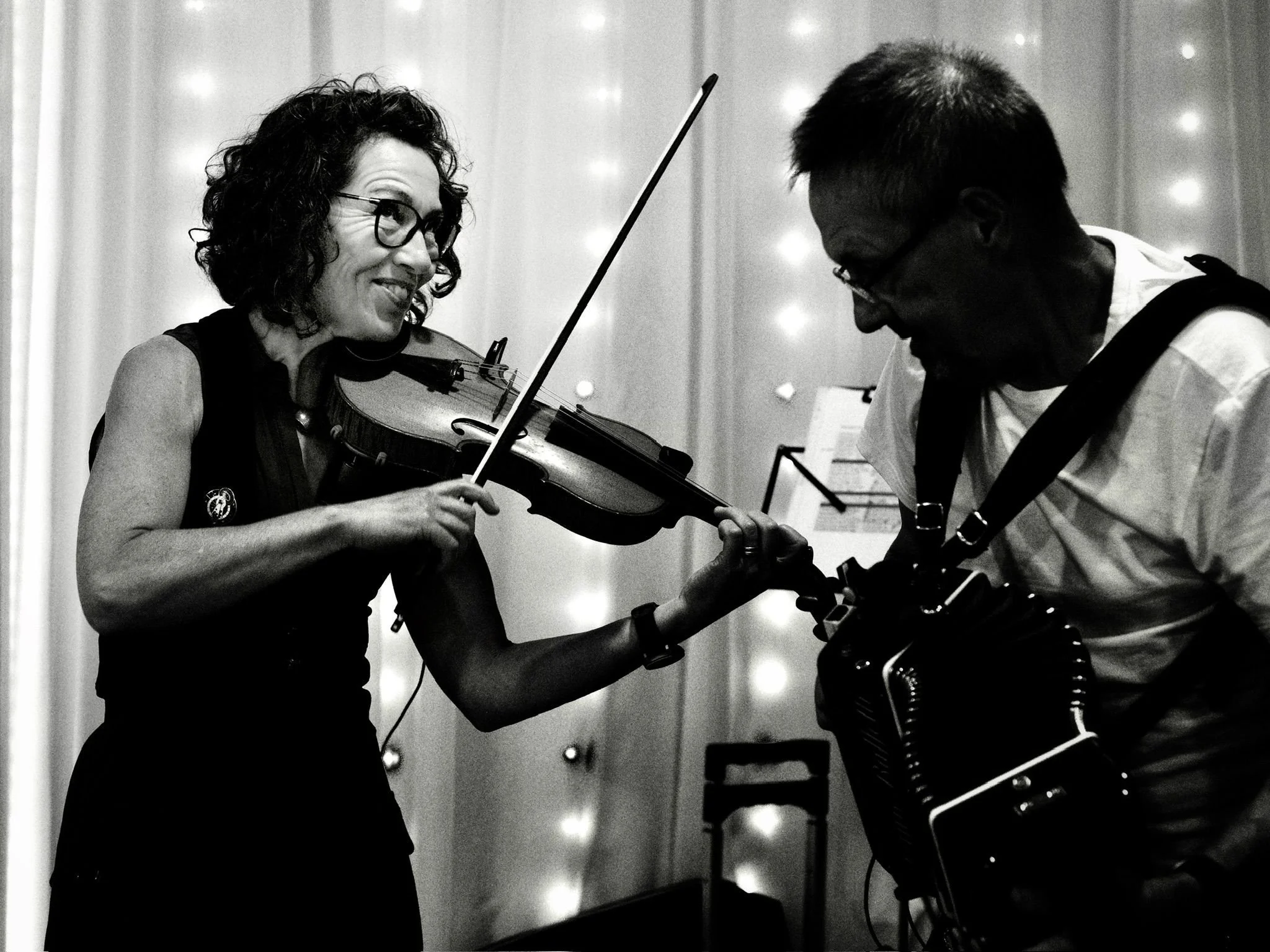 Woman playing the violin while a man with a camera captures the moment.
