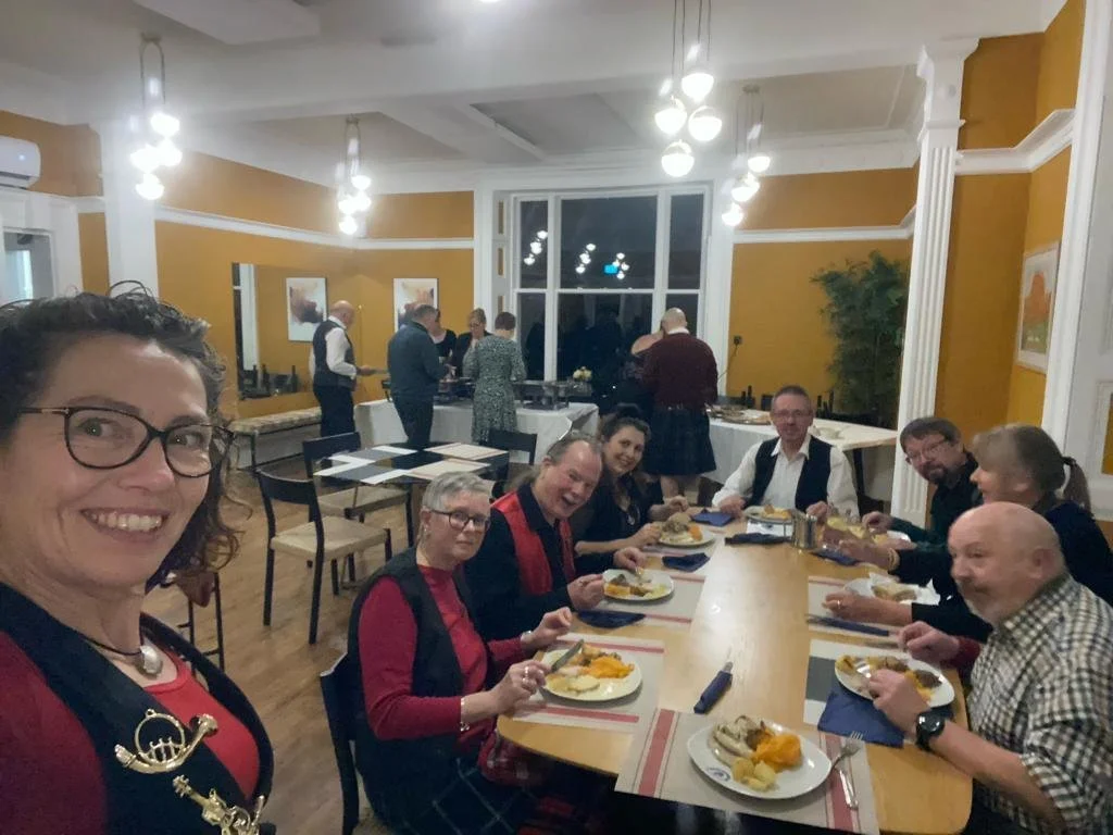 People gathered around a dining table enjoying a meal in a warmly decorated room with yellow walls, white trim, and modern lighting.
