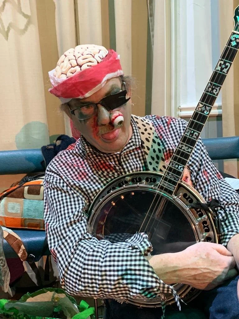 Person dressed as a clown playing a banjo, wearing a brain hat and clown makeup.