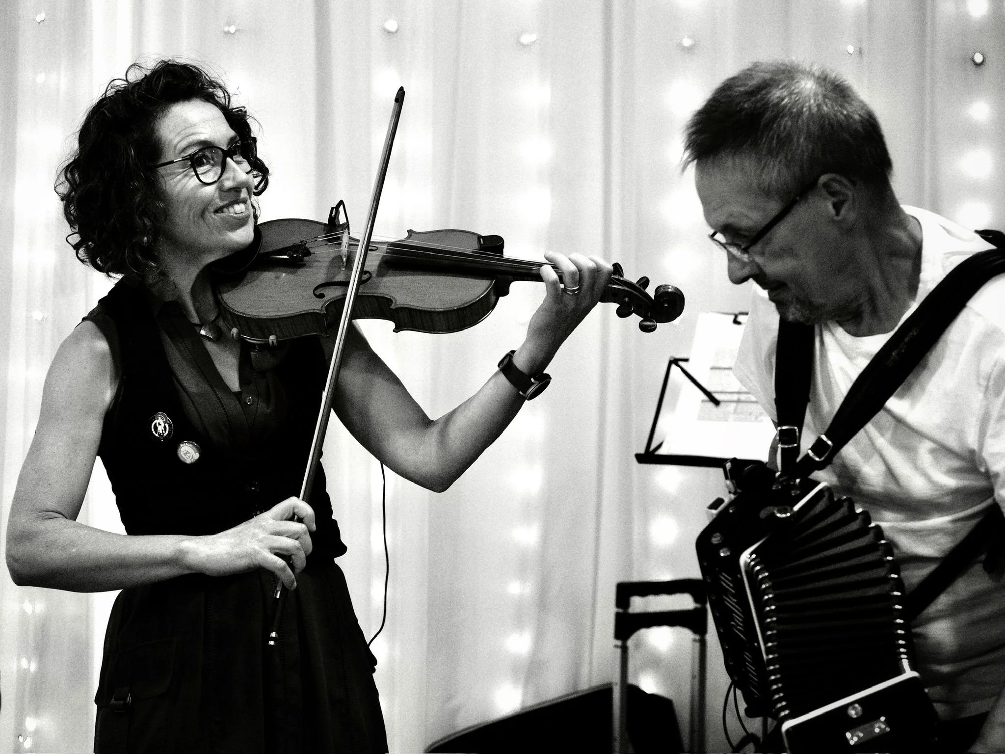 Woman playing violin and man playing accordion sharing a moment in a performance setting