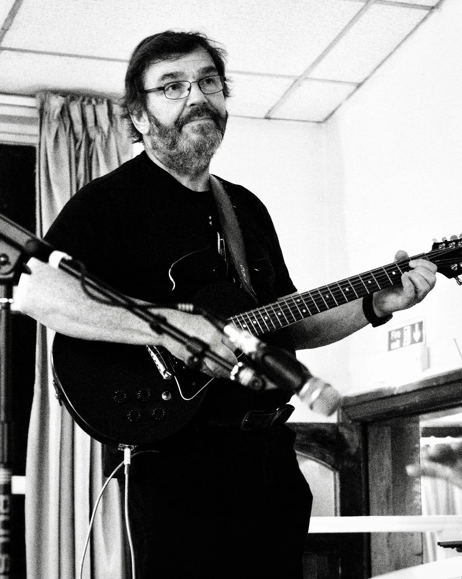 A man with glasses and a beard playing an electric guitar in a room.