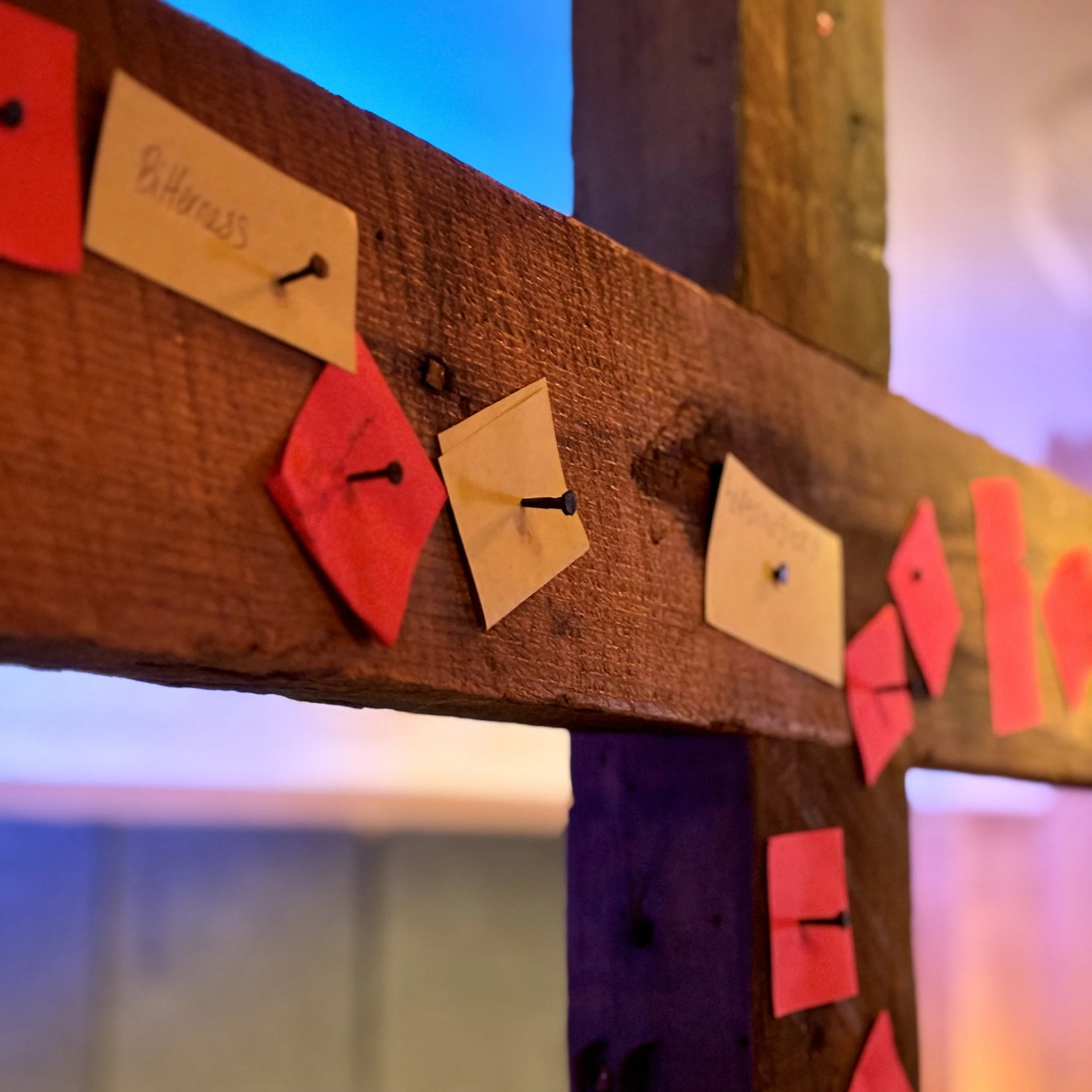 Close-up of a wooden surface with small red and cream-colored paper notes attached with nails, some of them have handwritten words, in a colorful indoor setting.