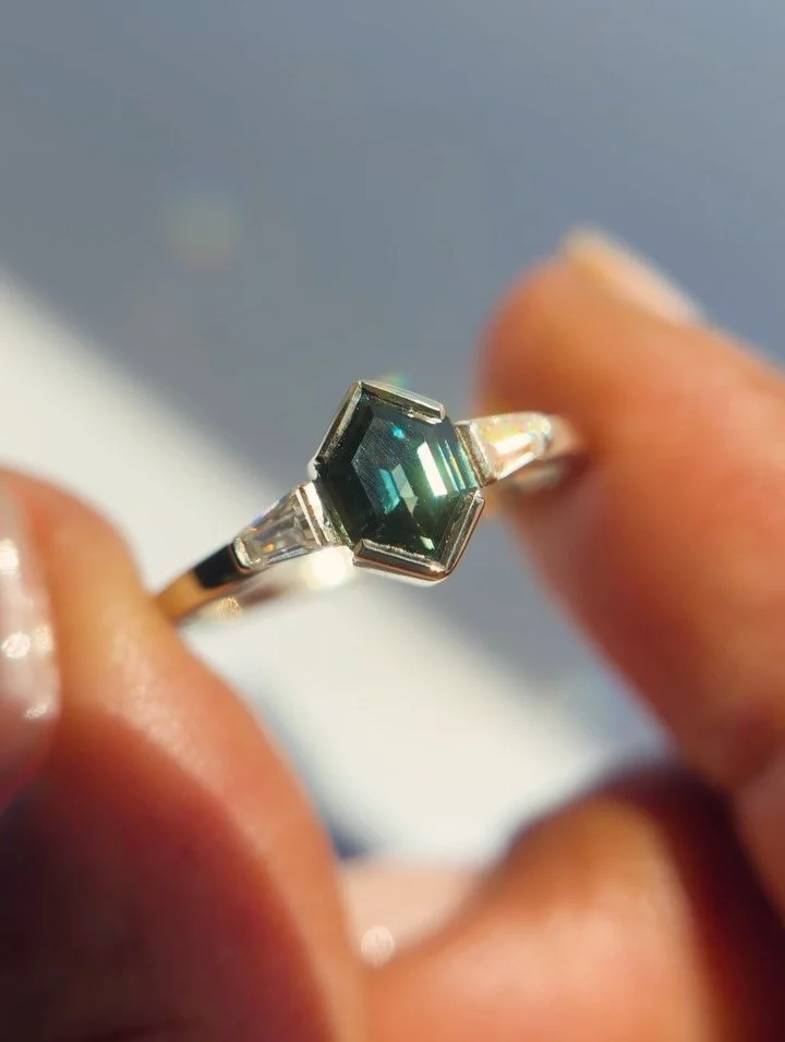 She said yes! 💍 How could you not when your partner secretly commissions a design this special? This non-traditional engagemnt ring features an elongated hex Australian Sapphire center stone and tapered baguette sides set in white gold. Thanks to my