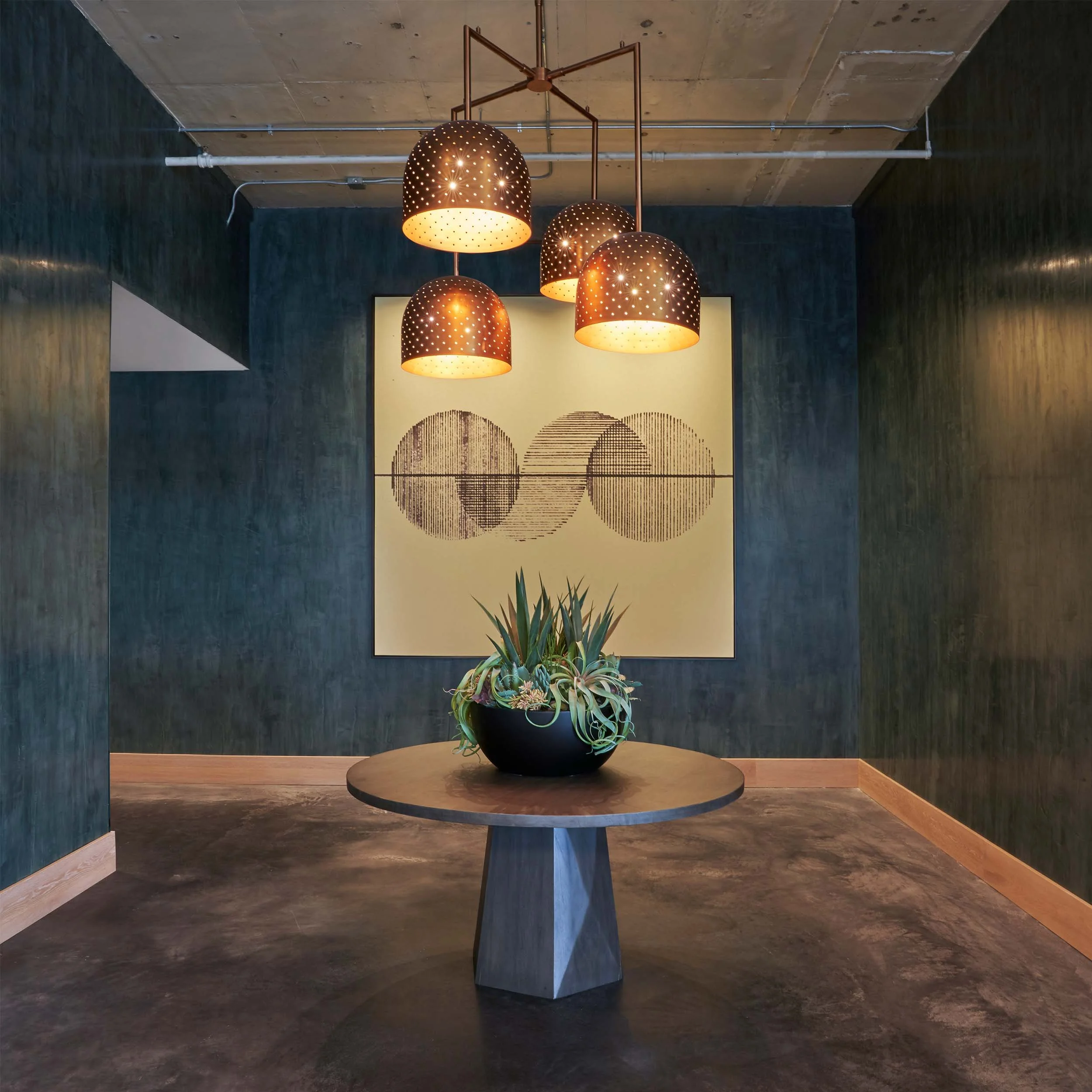 Green plaster walls, copper perforated light fixtures, oversized succulent planter on center lobby table.