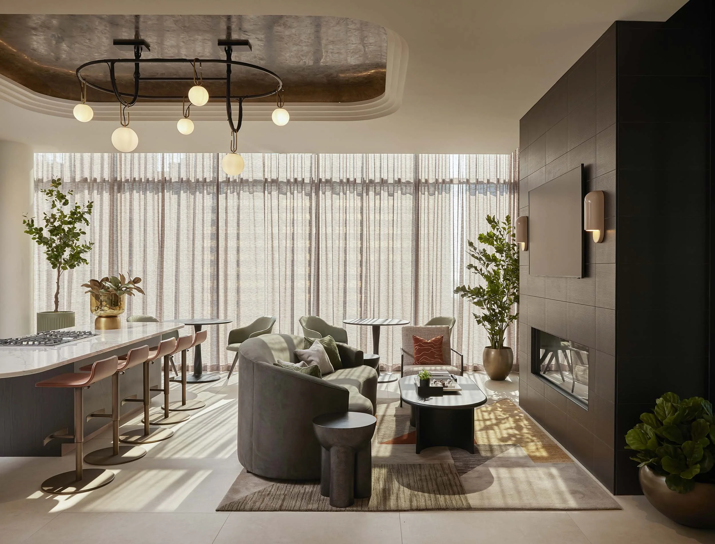Lounge with dark modern fireplace, curved sofa, and modern kitchen island with gold ceiling