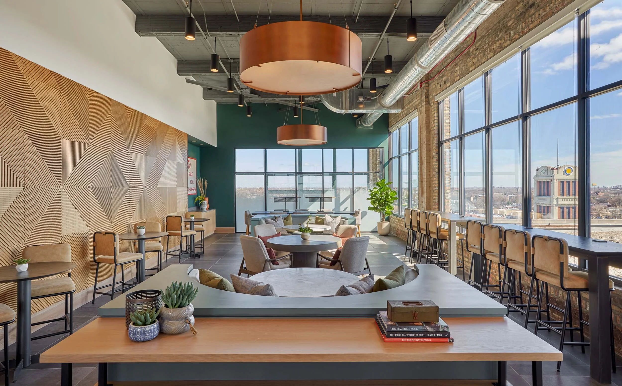 Coworking space with textural patterned wood wall, leather strapped barstools, communal table, round booths