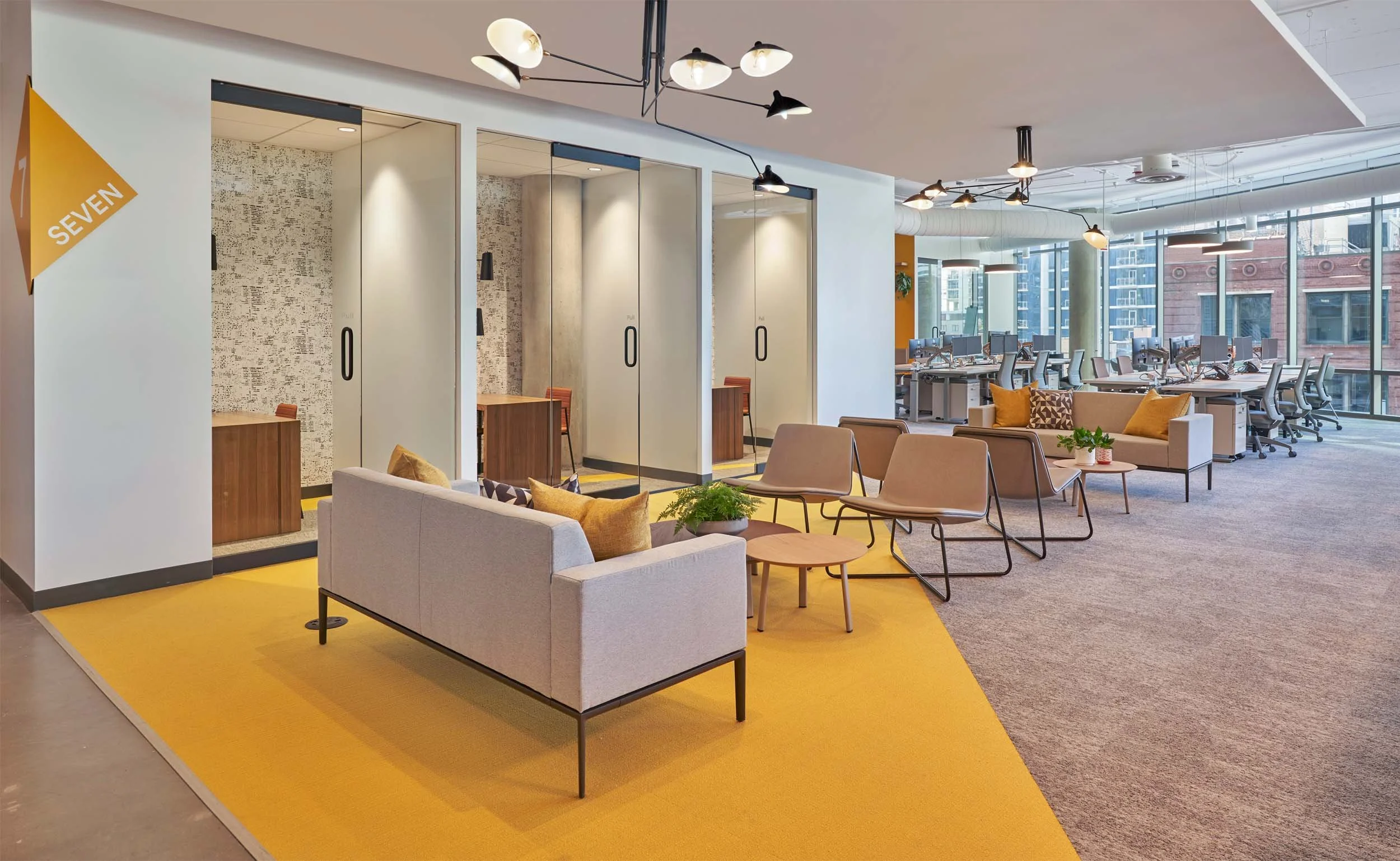Elevator lounge with glass phonebooths and desking systems beyond. Modern punches of color pulled from brand packaging