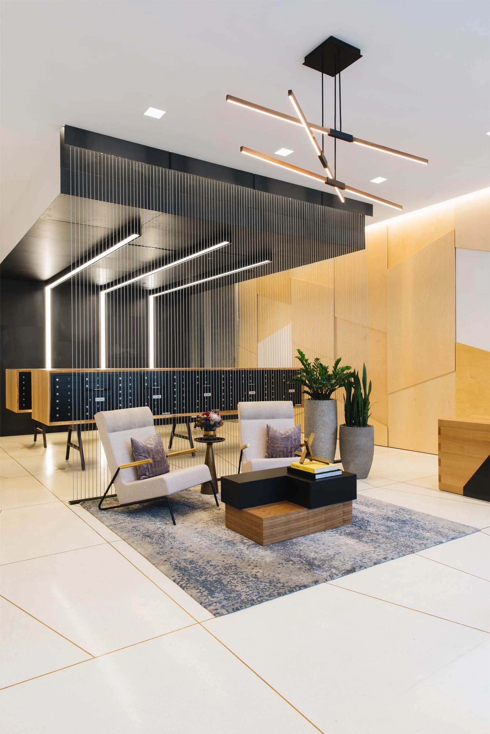 Modern lobby with geometric wood wall panels, freestanding mailboxes, and metal screen.