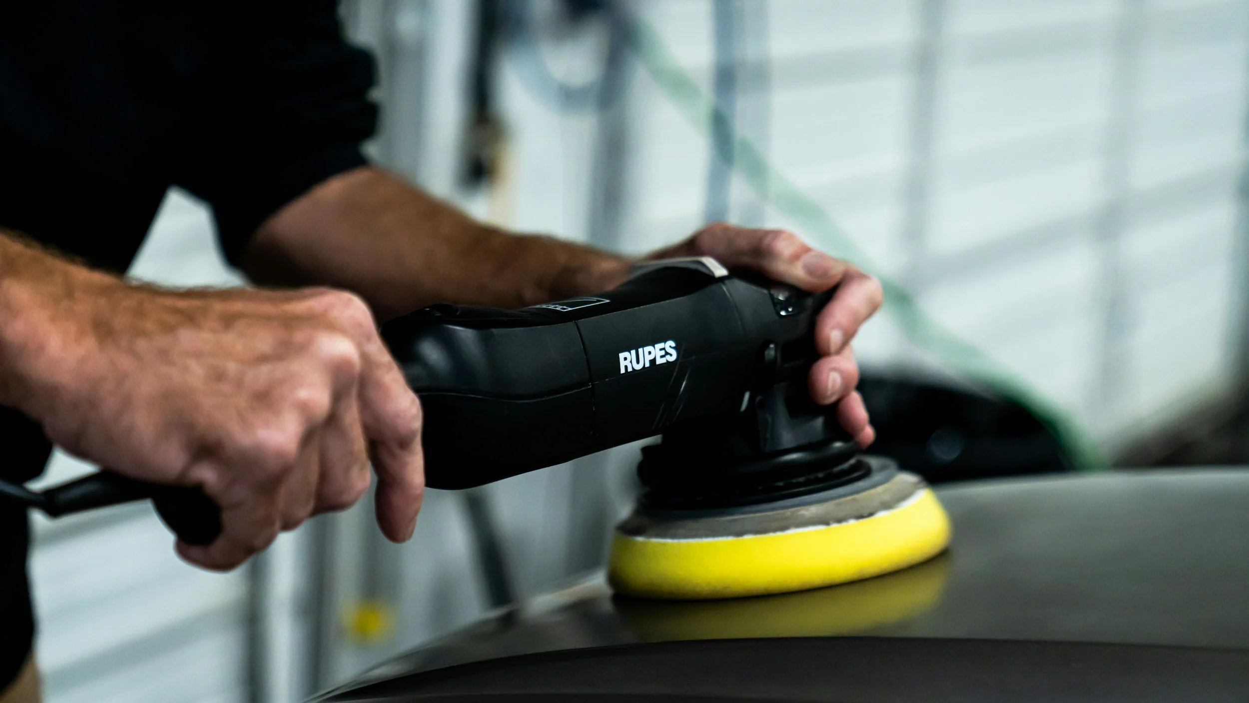 Close-up of a person's hands using a power buffer or polisher on a surface.