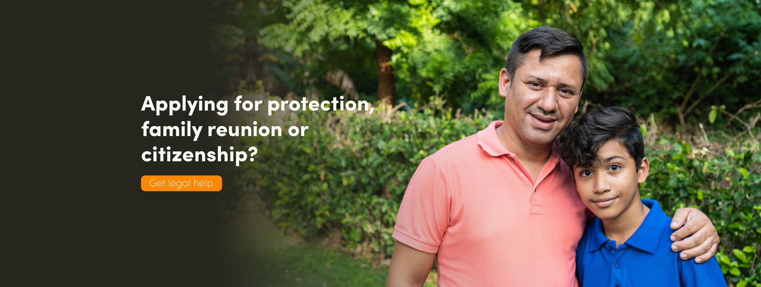 A smiling man in a pink shirt has his arm around his son, wearing a blue shirt.