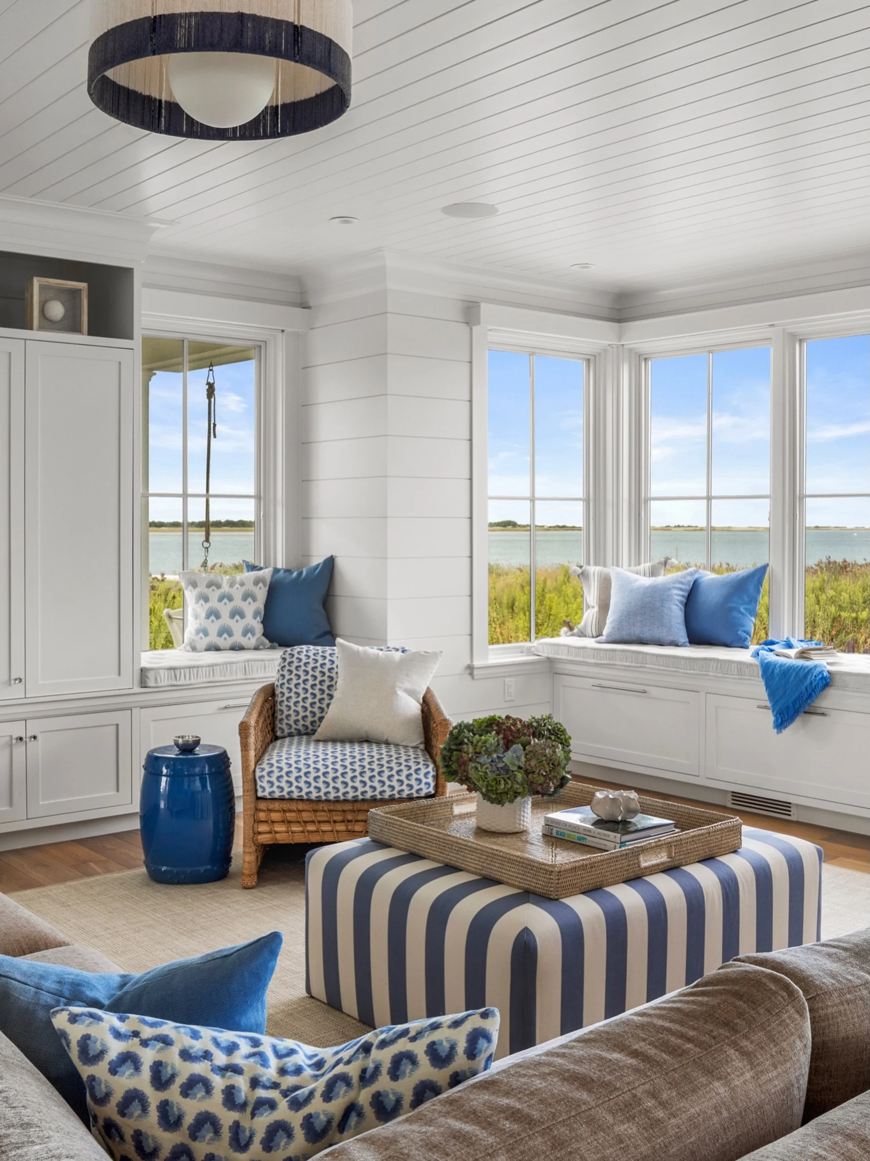 Coastal, carefree, and quietly colorful. Designed with connection in mind, this living room invites gathering while taking in the coastal views. A soft palette of beige, white, and blue sets the tone, with stripes and patterns layered throughout for 
