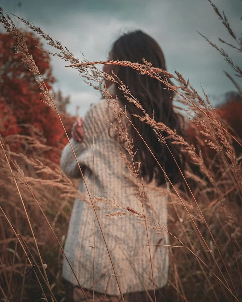 A woman standing outdoors among tall dry grasses wearing a beige sweater, representing grounding and connection to nature