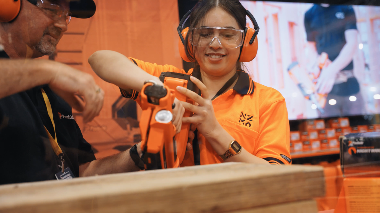 A Bunnings staff member trying a power tool with a supplier's guidance at the Bunnings Trade Expo