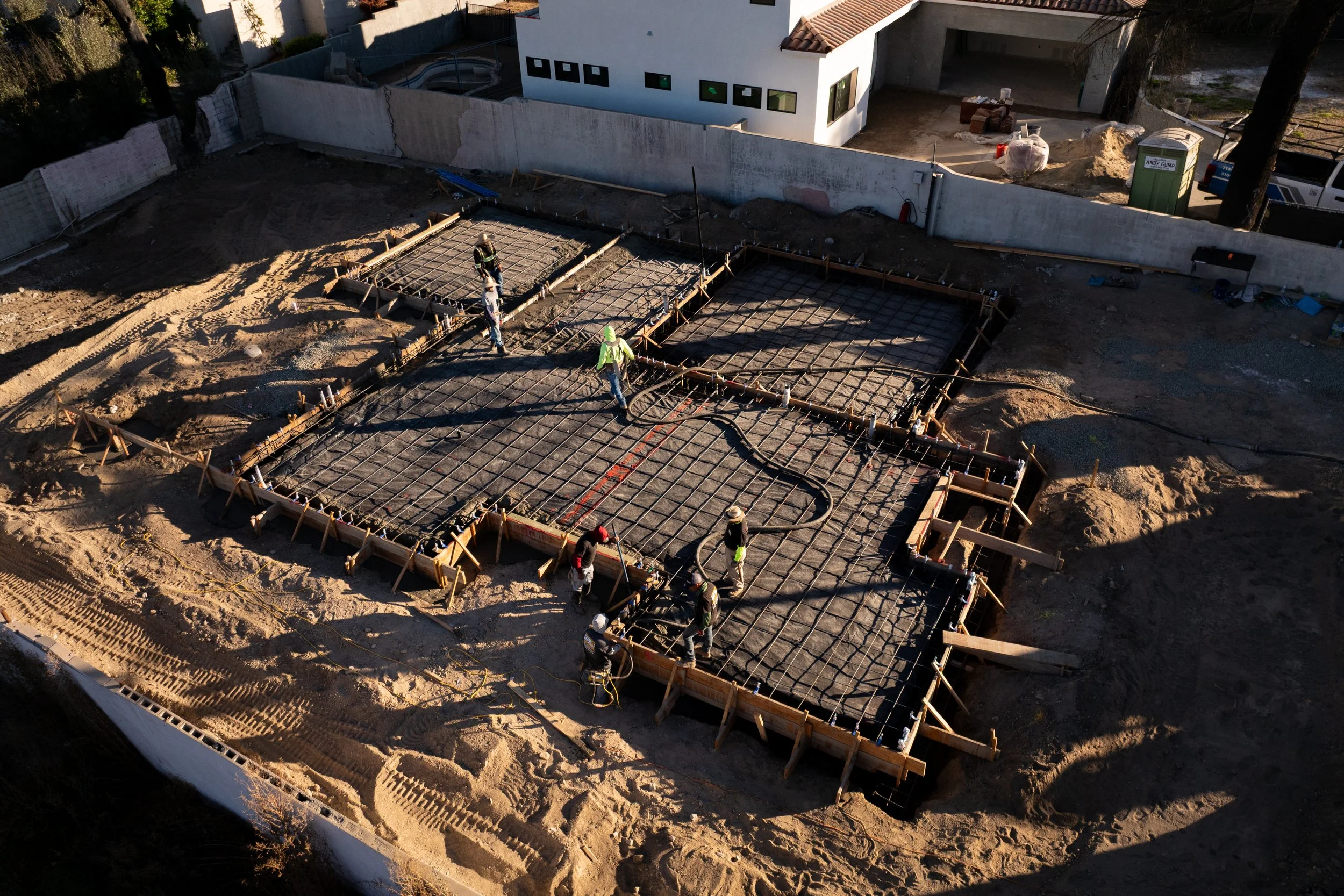 Construction workers are building a concrete foundation on a construction site, surrounded by dirt and wooden formwork.