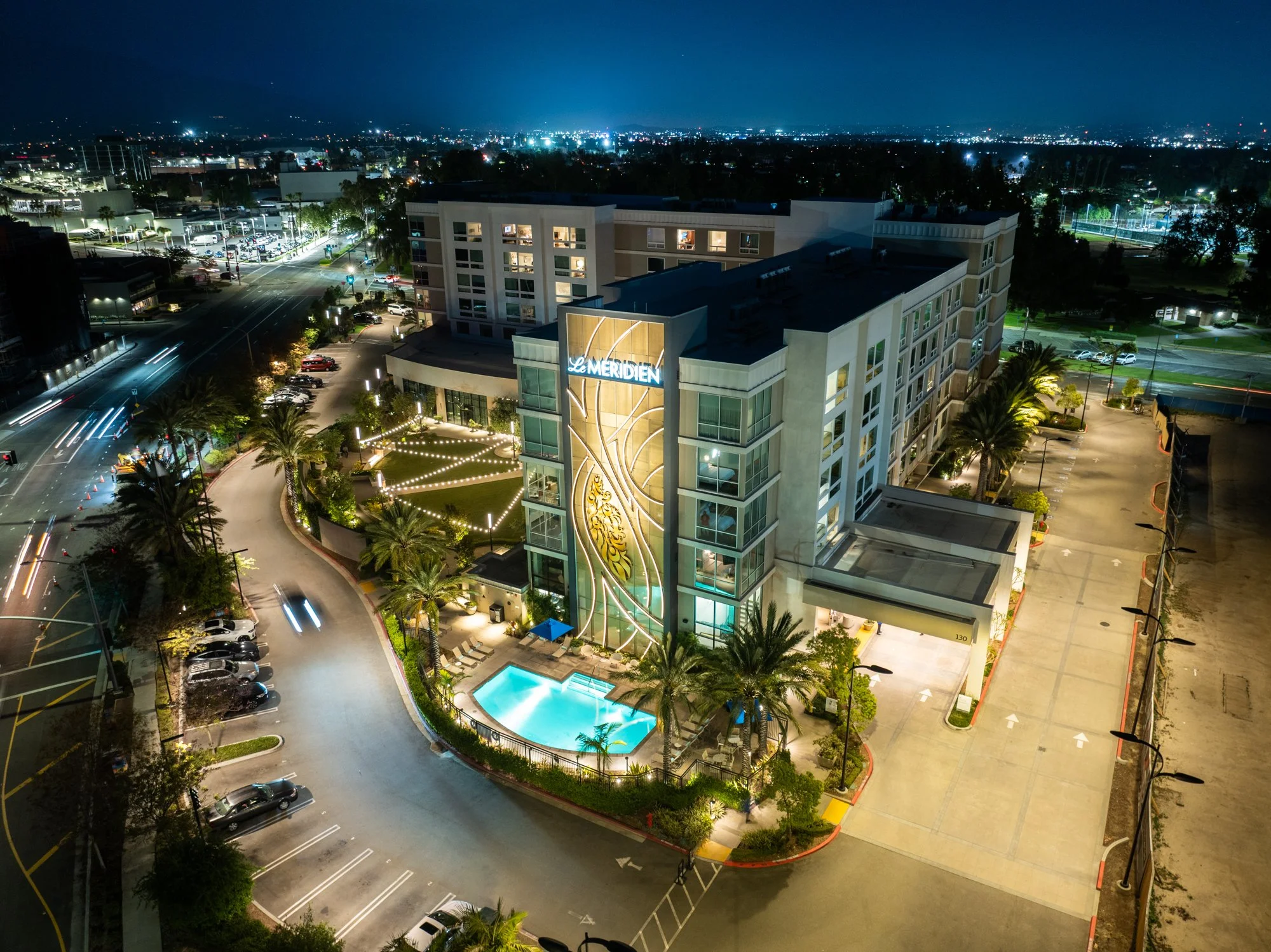 A modern house with wooden and stone exterior walls sits on a hillside in front of snow-capped mountains under a cloudy sky.