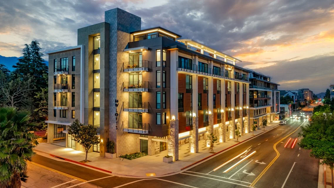 A modern multi-story building at sunset with exterior lighting, balconies, and large windows.