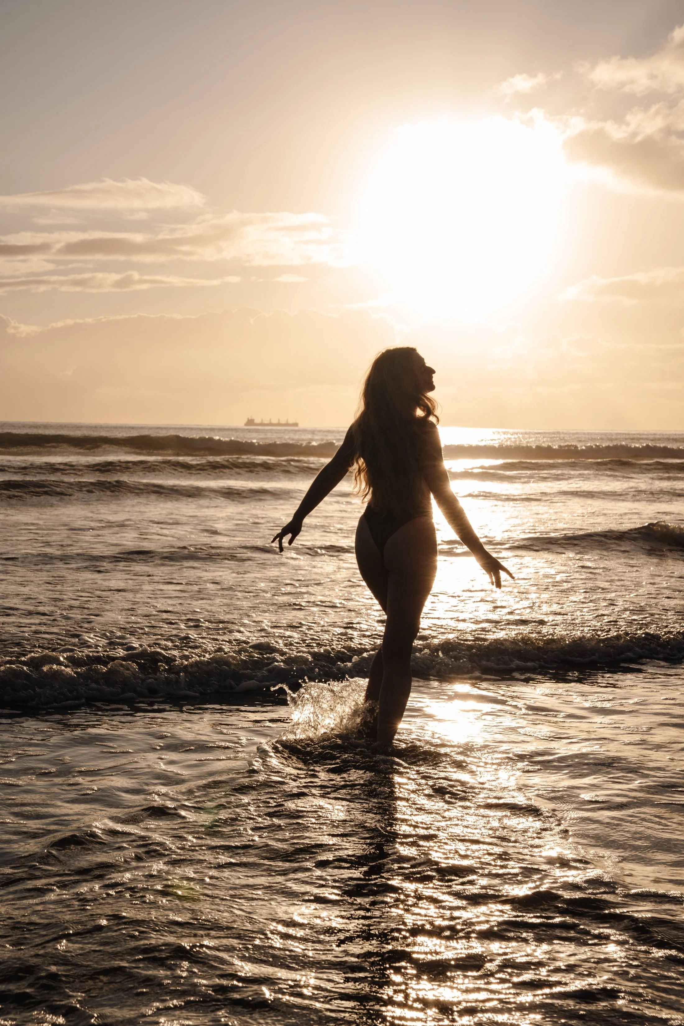 Silhouette of Sandrina running through the waves in front of golden sunrise