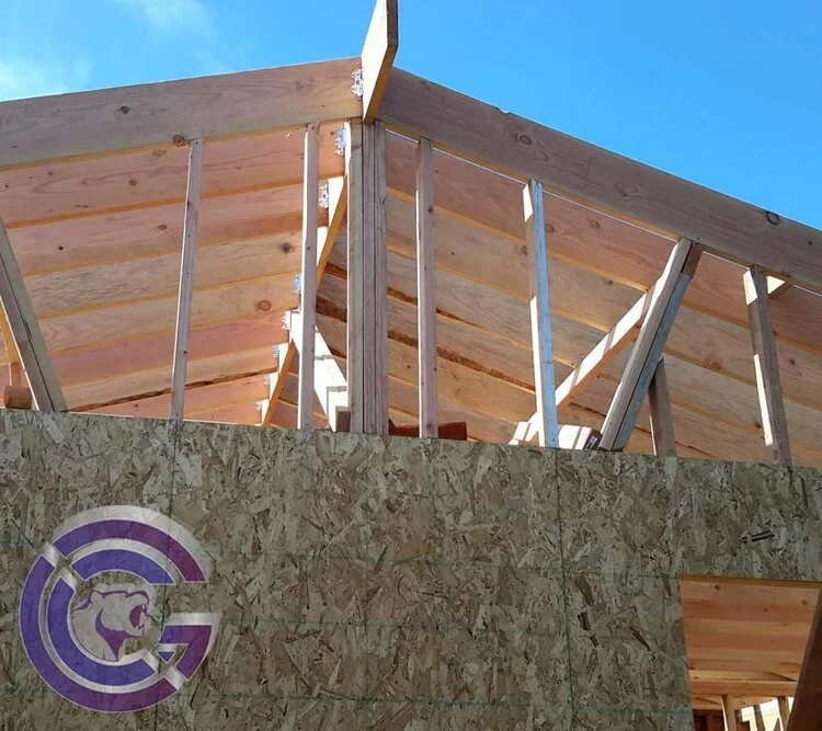 Construction site with wooden framing and plywood siding, part of a building under construction, with a clear blue sky in the background.