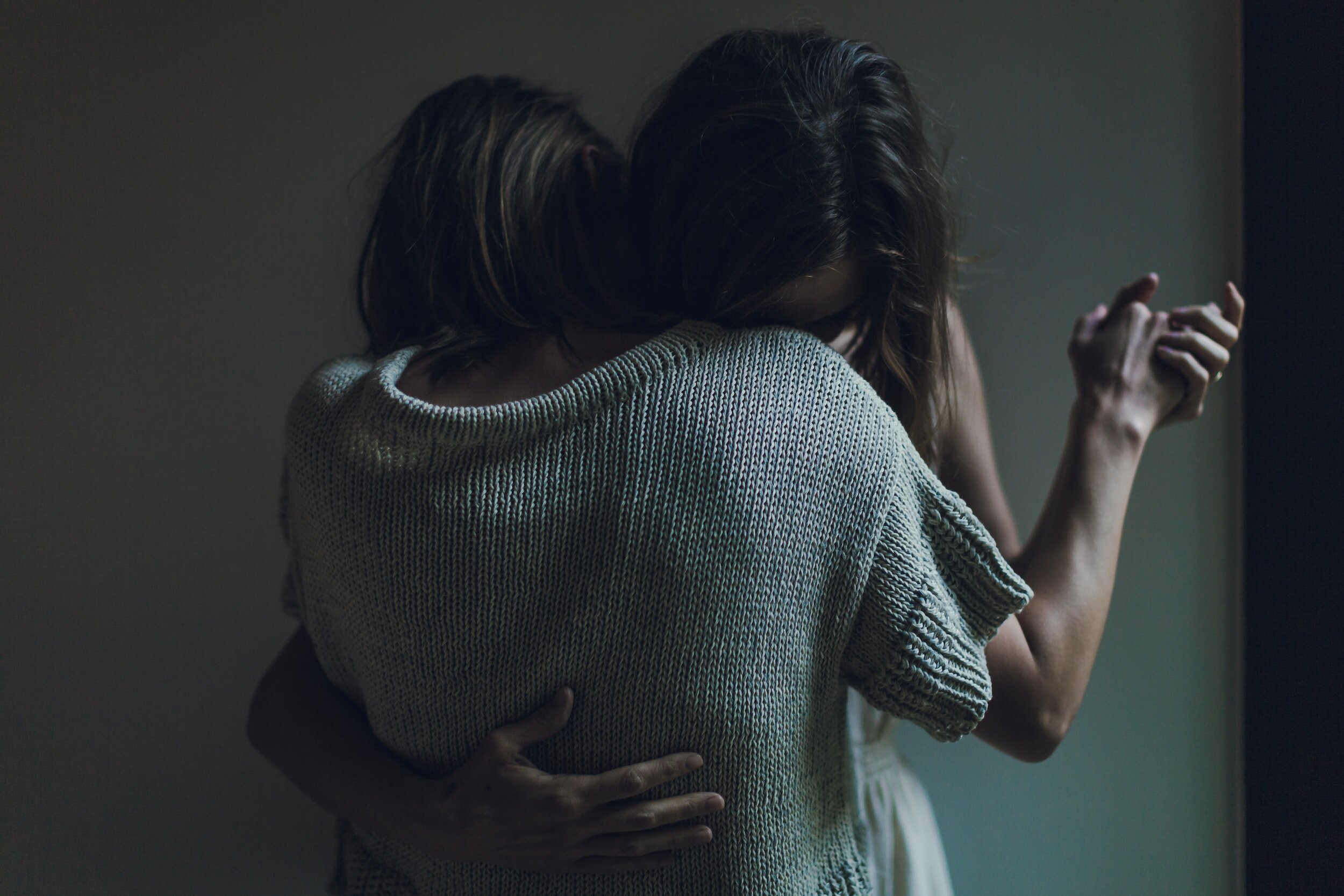Two women embracing in a comforting hug, with one woman gently holding the other who has her eyes closed.