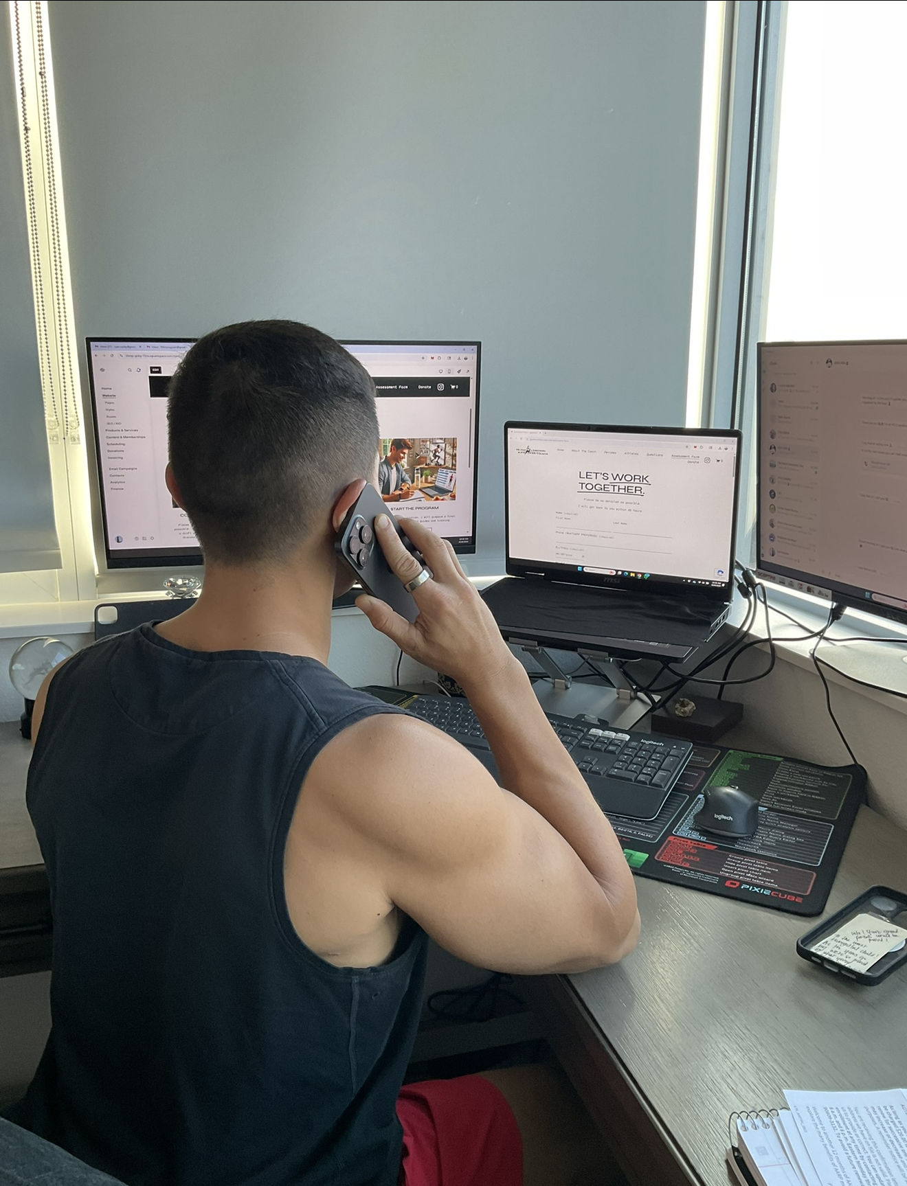 A man sitting at a desk talking on the phone in front of three computer monitors.