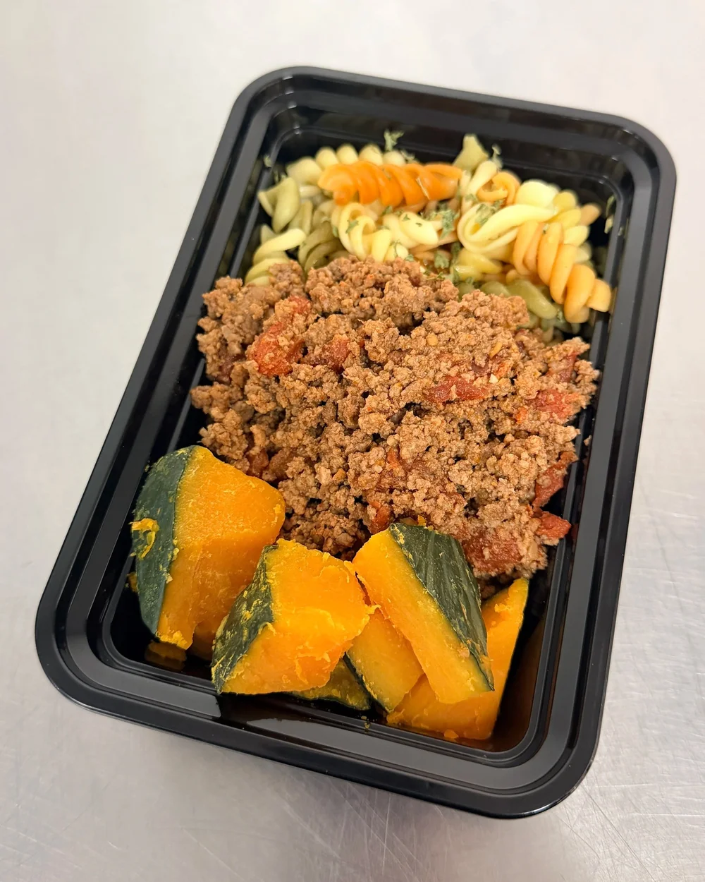 FFYG meal with seasoned ground beef, pasta and roasted squash in a black meal prep tray