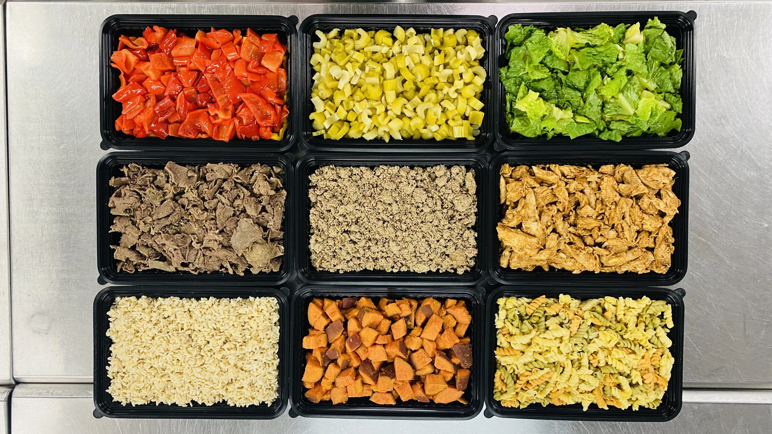 A top-down view of nine black takeout containers filled with various chopped vegetables and cooked ingredients, arranged on a stainless steel surface.