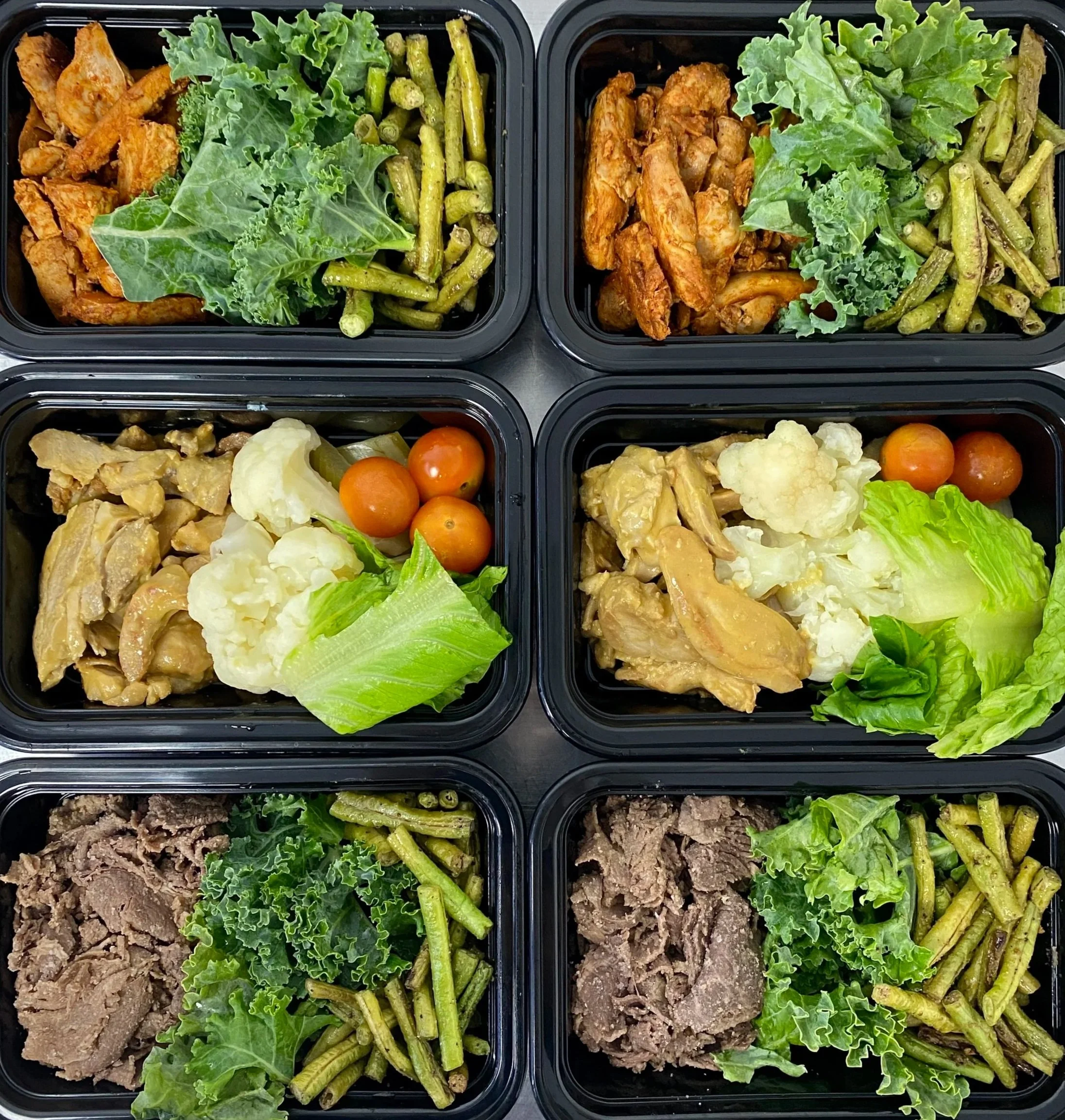 Eight meal prep containers arranged in two rows of four, each filled with different portions of cooked meat, vegetables, and greens, including chicken, beef, cauliflower, cherry tomatoes, green beans, lettuce, and kale.