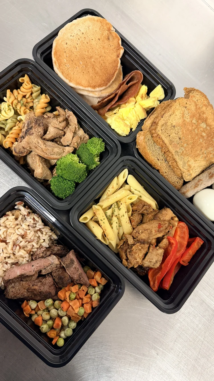Meal containers with pasta, roasted vegetables, chicken, rice, beef and a breakfast sandwich