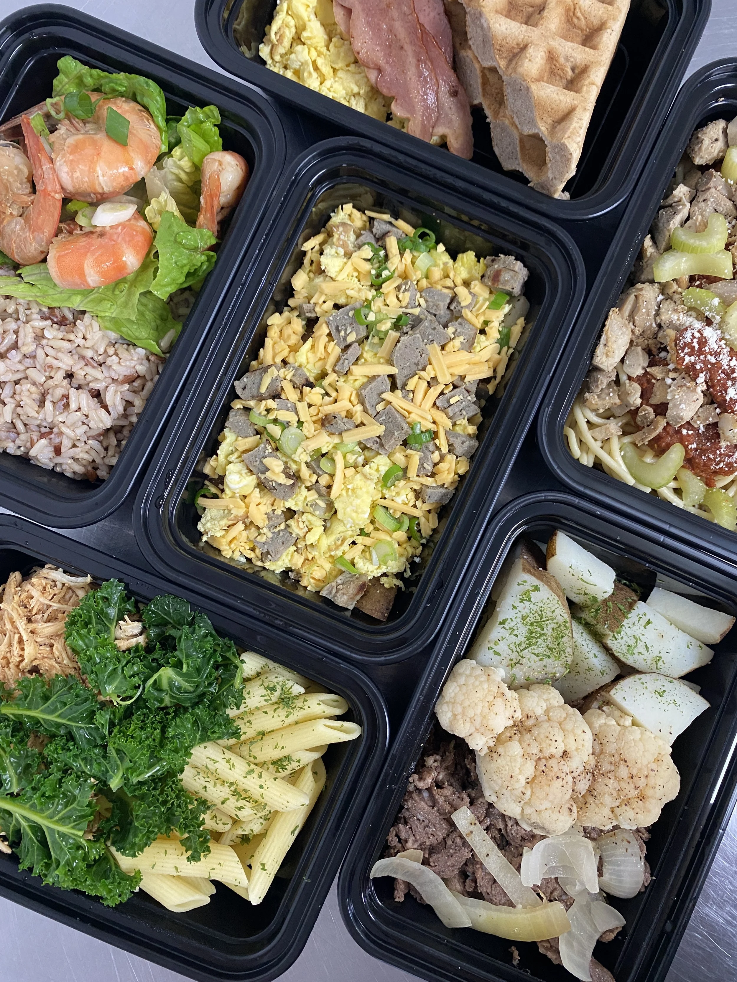 Meal prep containers with shrimp salad, scrambled eggs with cheese and green onions, bacon, pasta with kale and tuna, cauliflower, and beef with onions.