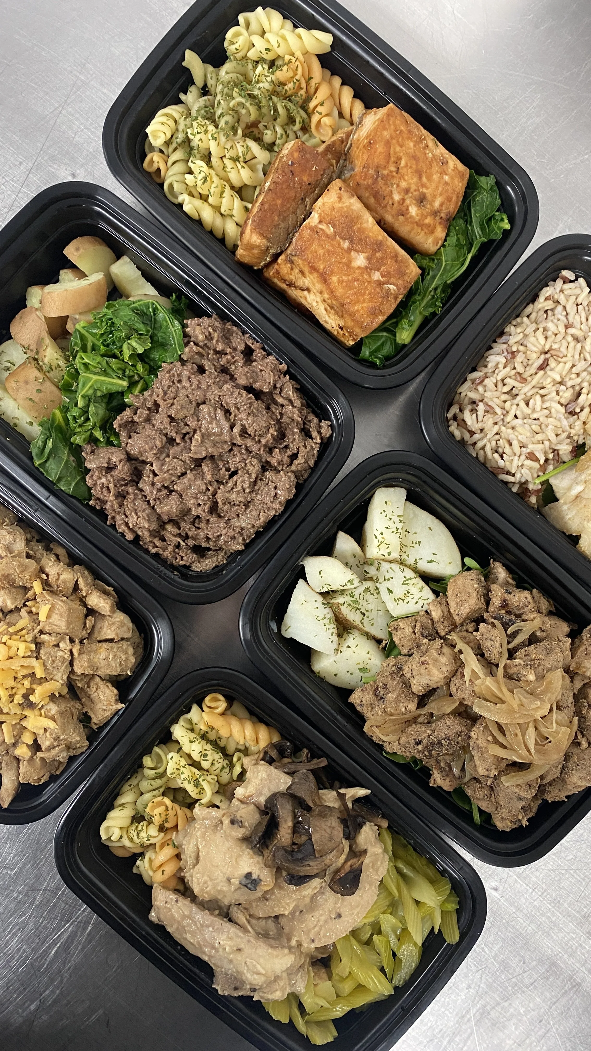 Four meal prep containers with pasta, grilled salmon, ground beef, potatoes, and vegetables.