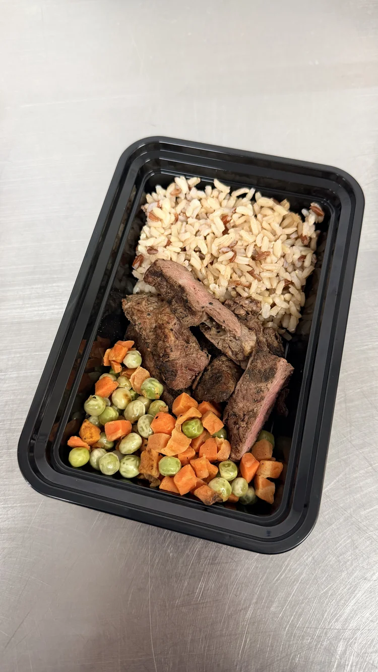 Meal prep container with rice, grilled beef ribs and mixed peas and carrots