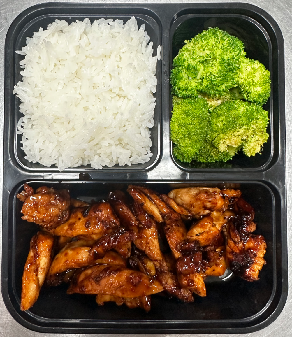A divided black meal tray with white rice, steamed broccoli, and glazed chicken wings.