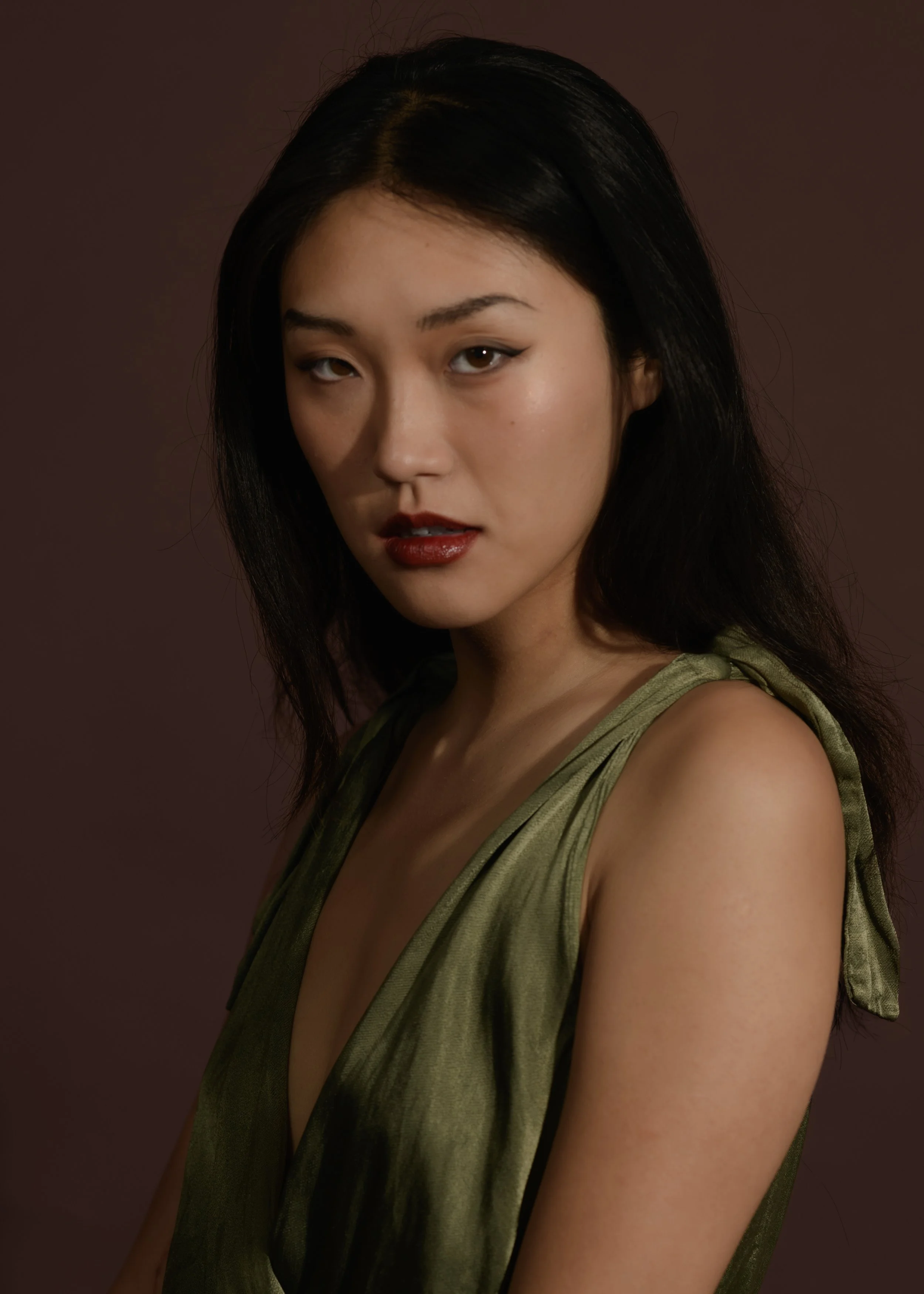 Portrait of a woman with long dark hair, wearing a green satin dress against a brown background.