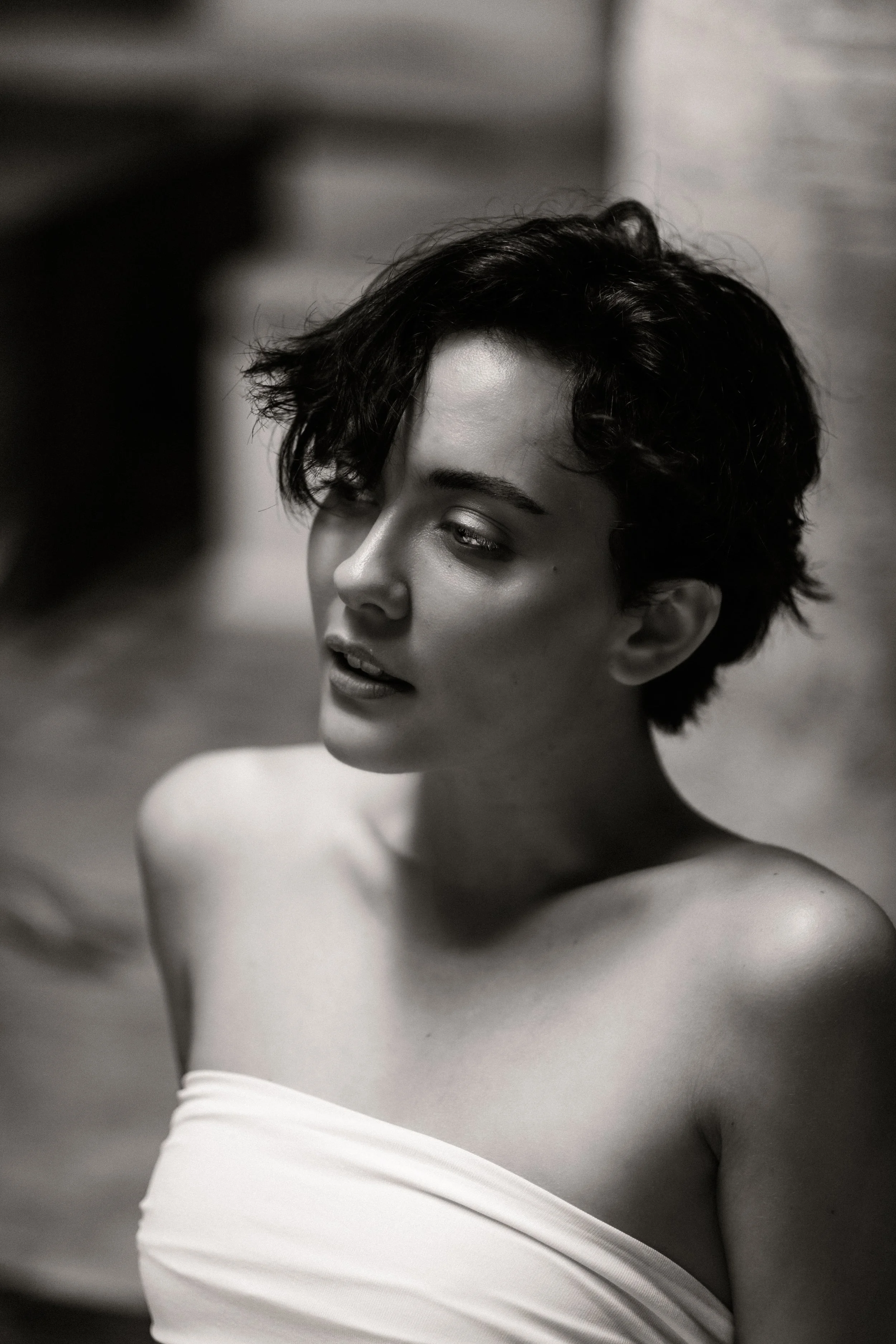 Black and white portrait of a woman with short, wavy hair, looking contemplative, wearing a white top.