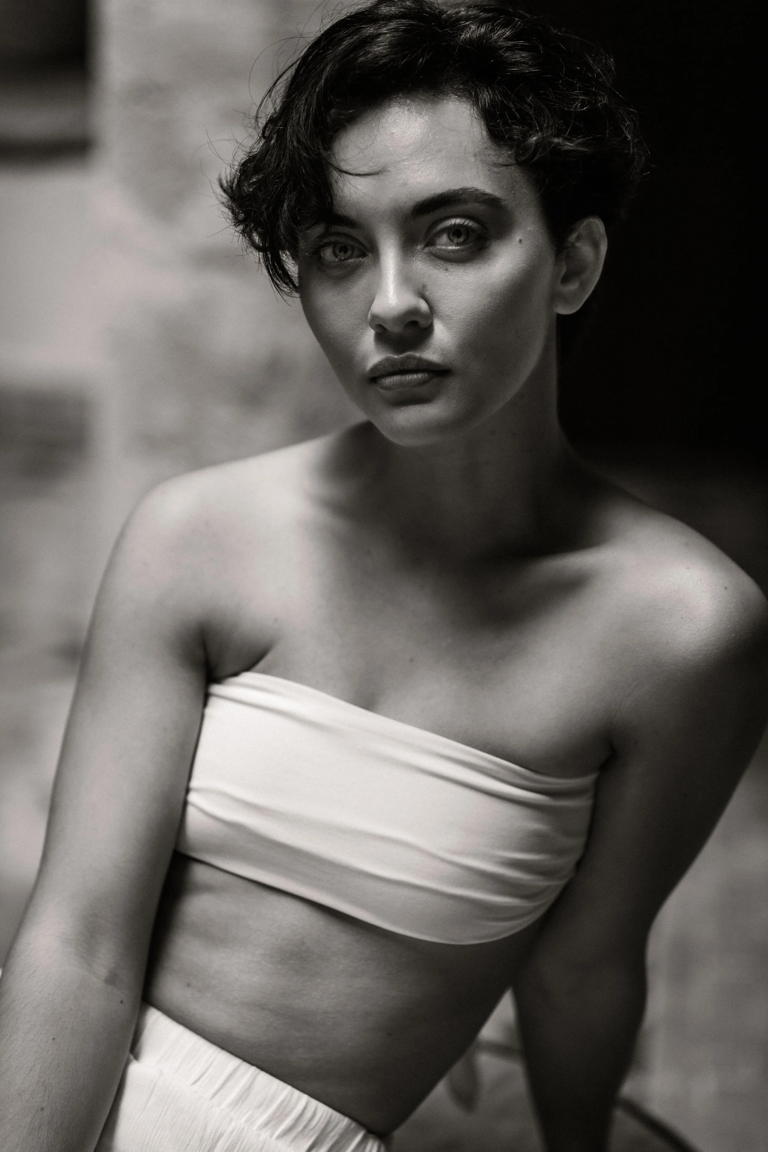 Black and white photo of a woman with short curly hair, wearing a strapless top, looking directly at the camera with serious expression.