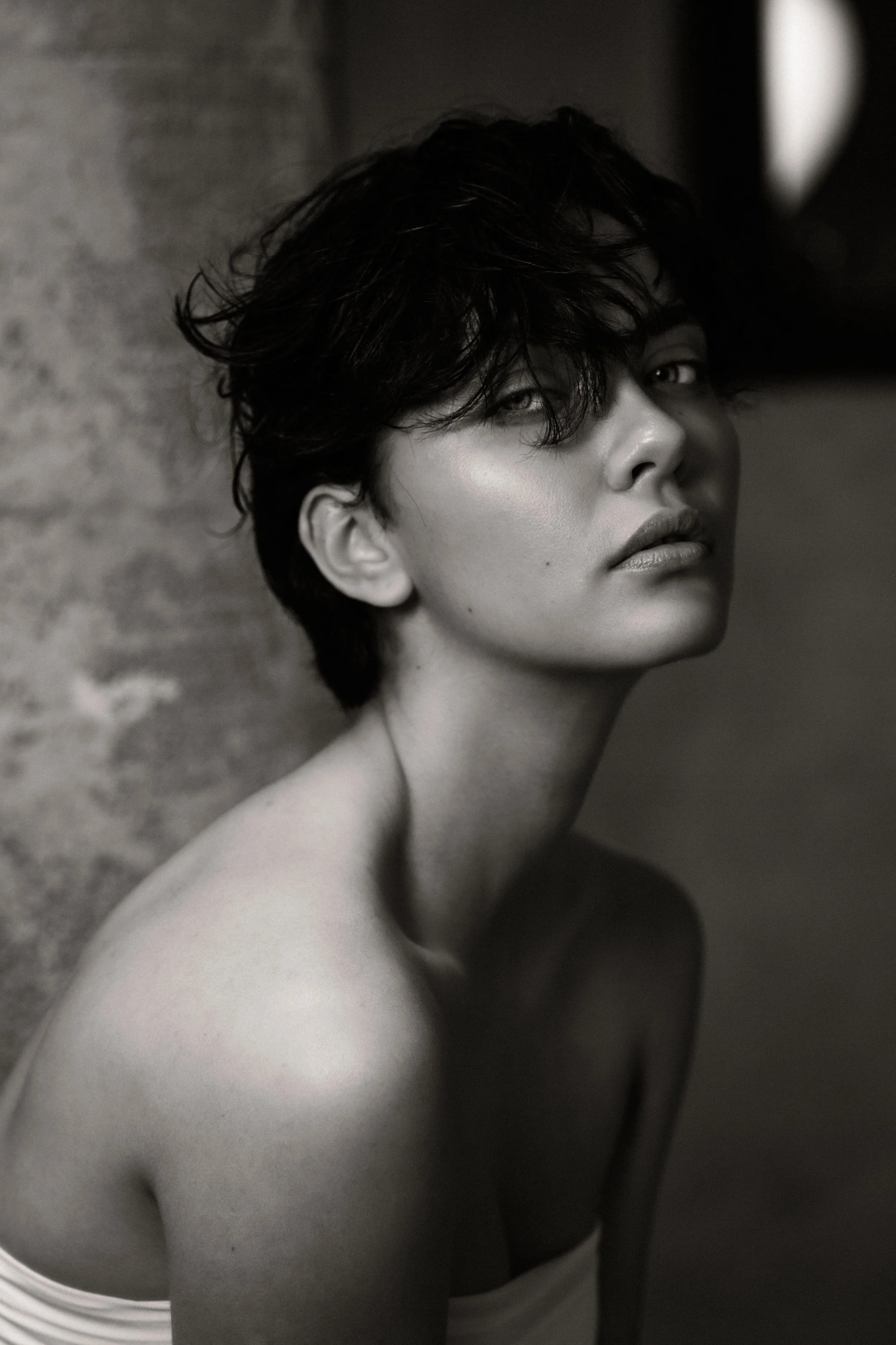 Black and white close-up portrait of a young woman with short wavy hair and a serious expression, looking slightly off-camera.