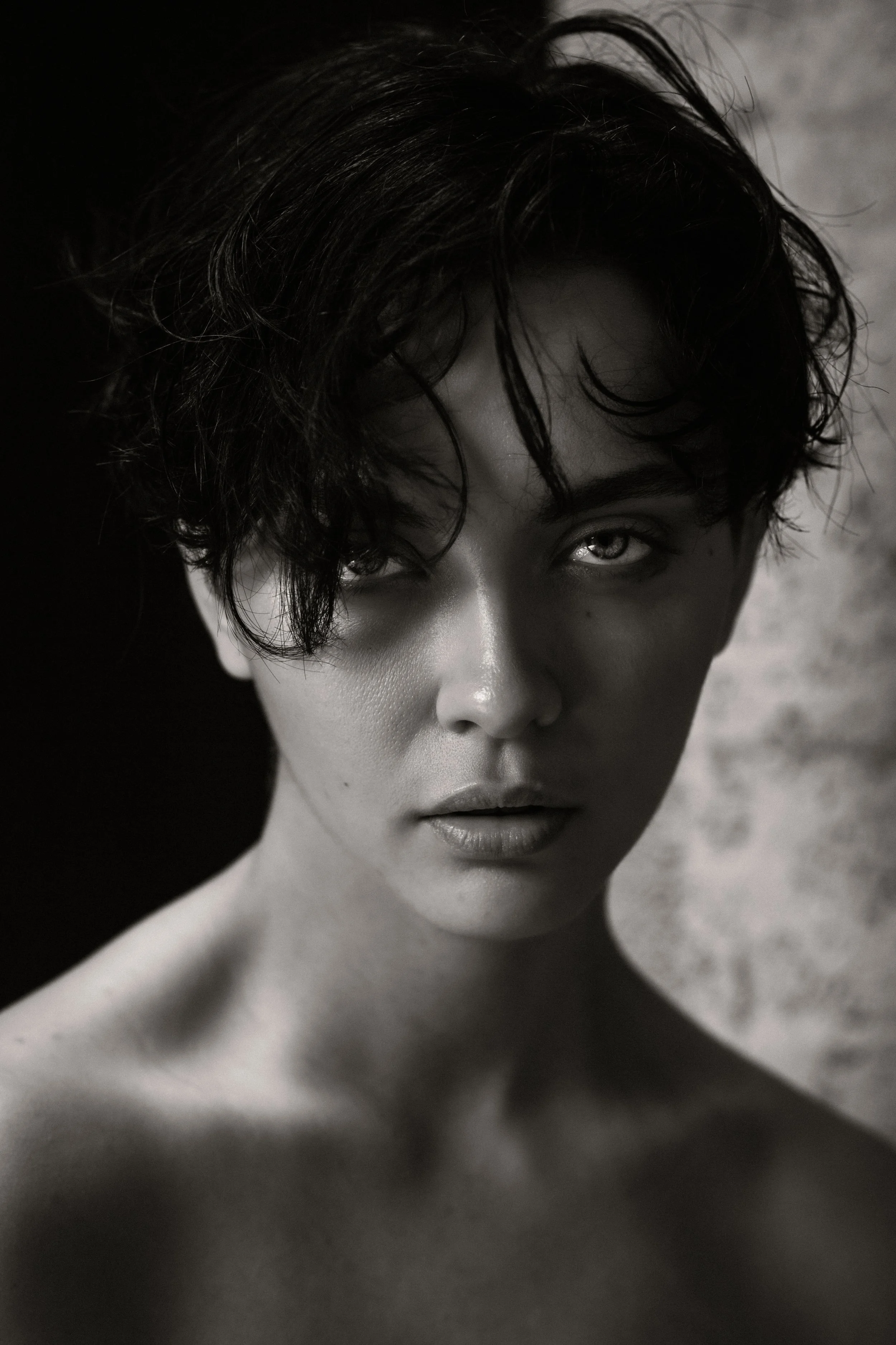 Black and white portrait of a woman with short wavy hair, gazing directly at the camera, with the focus on her face and neck.