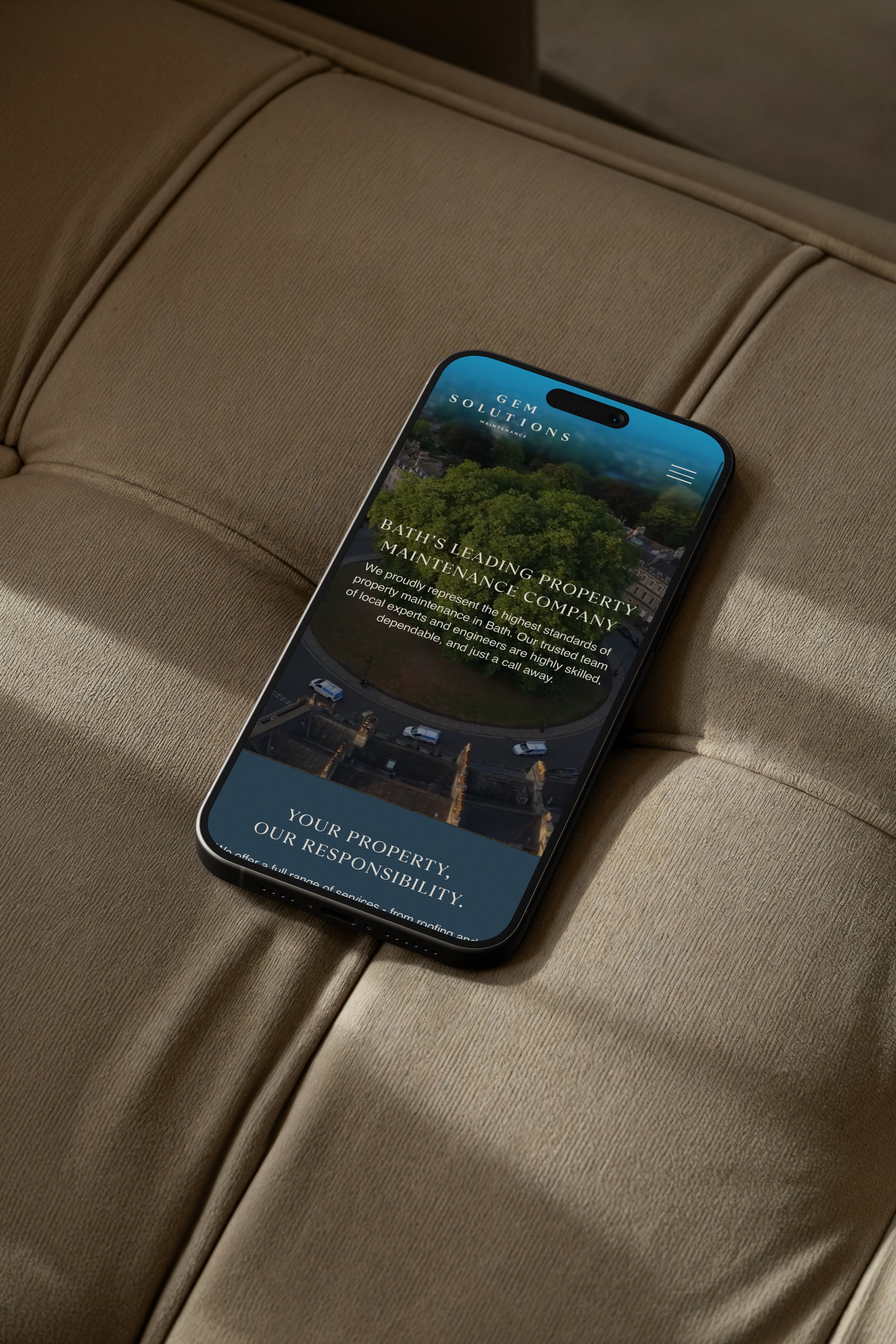 Smartphone displaying a website for GEM Solutions with information about bath maintenance services, resting on a beige upholstered surface.