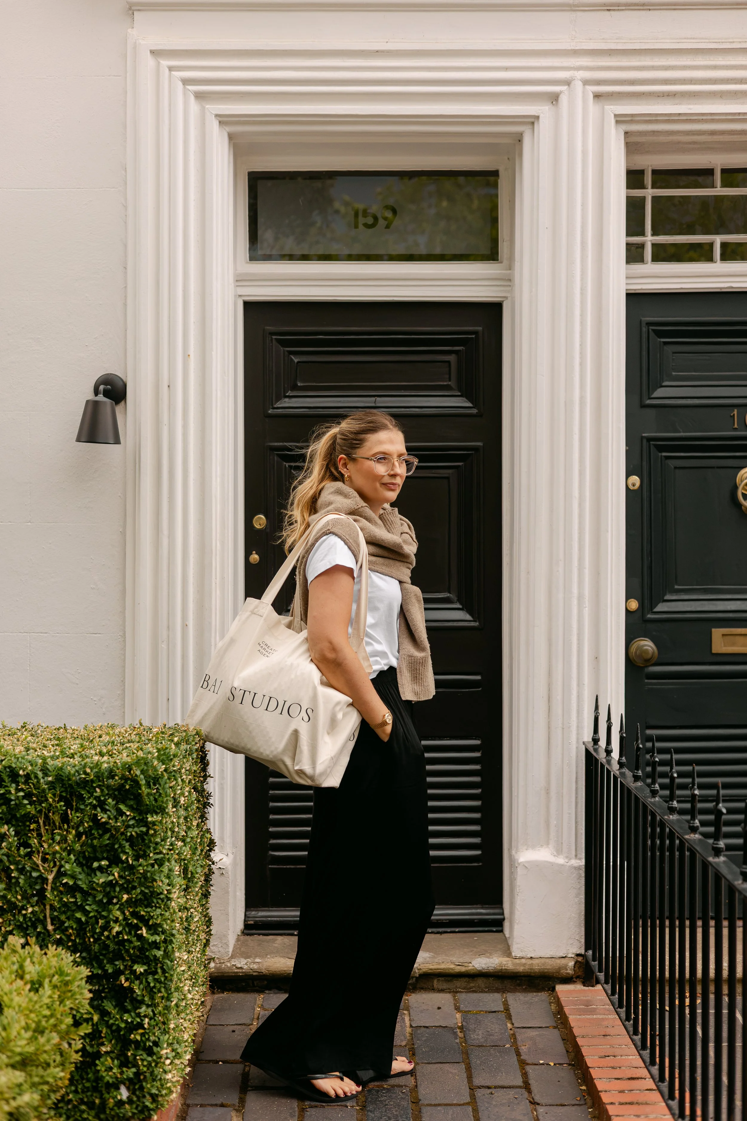 Woman standing in front of premium property, carrying a large branded tote bag with BA1 Studios on the bag.