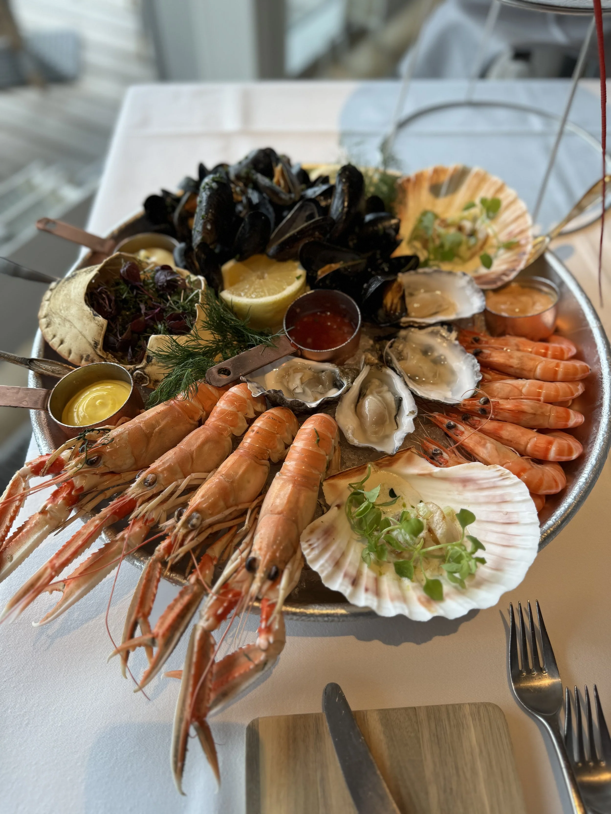 Skaldyrssæt med hummer, rejer, østers, muslinger og muslingesalat serveret på fad med tilbehør og citrondelender.
