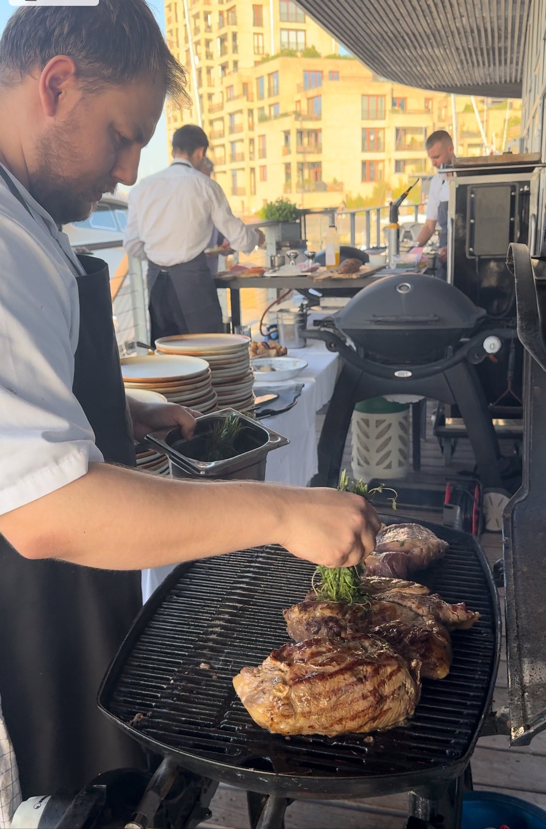 Kokke griller kød på en udendørs grill.