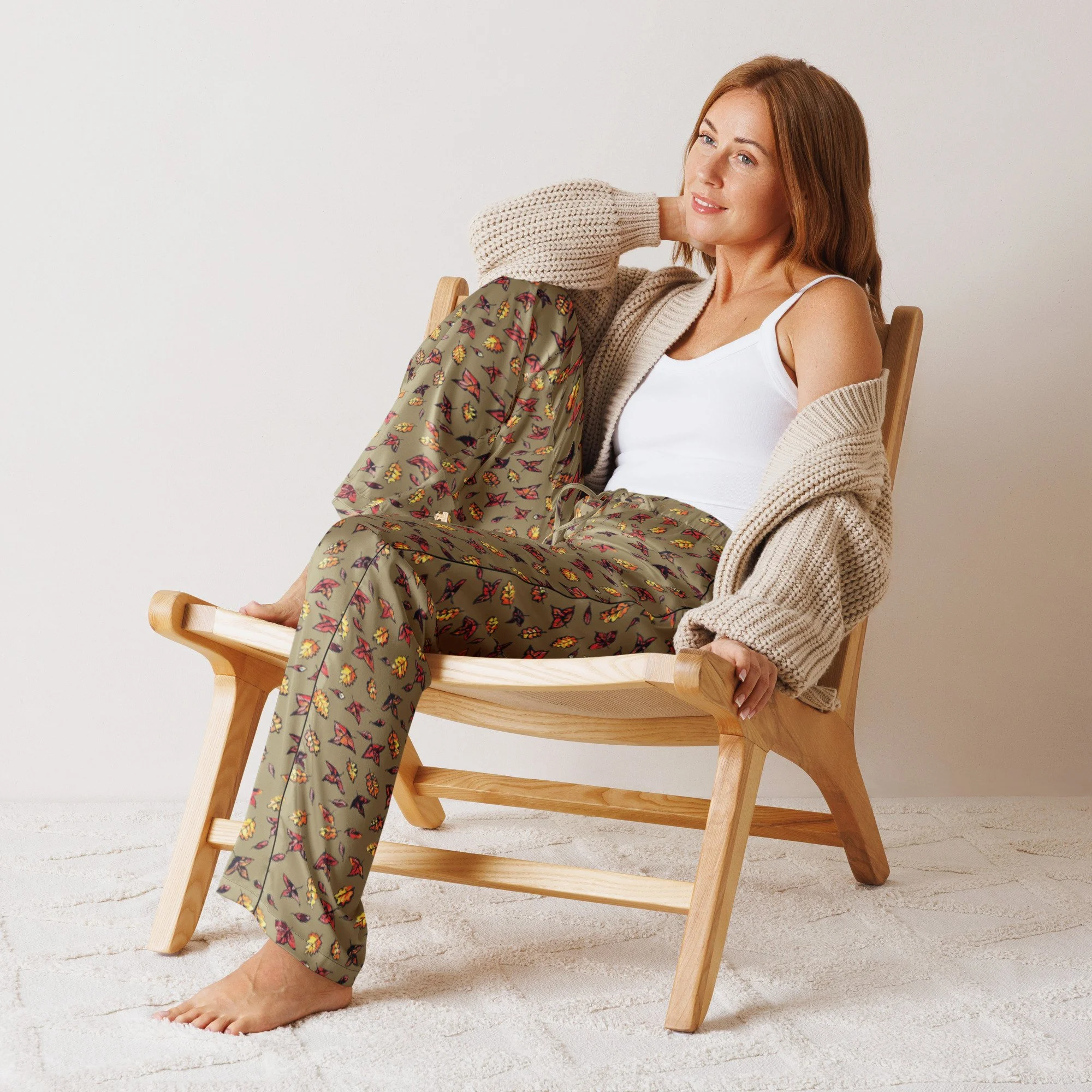 Woman relaxing in a wooden chair in the Autumn Green silky pyjama trousers