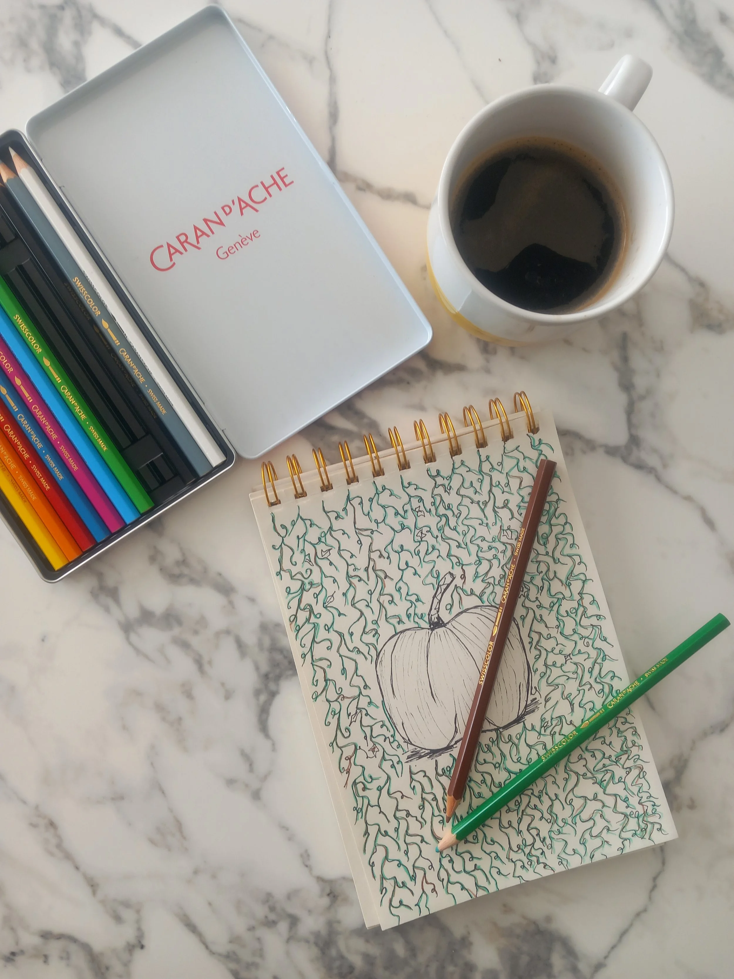 Hand-drawn pumpkin sketch on a spiral notebook with coloured pencils and coffee, showing The Nymph Anthologie's original design process