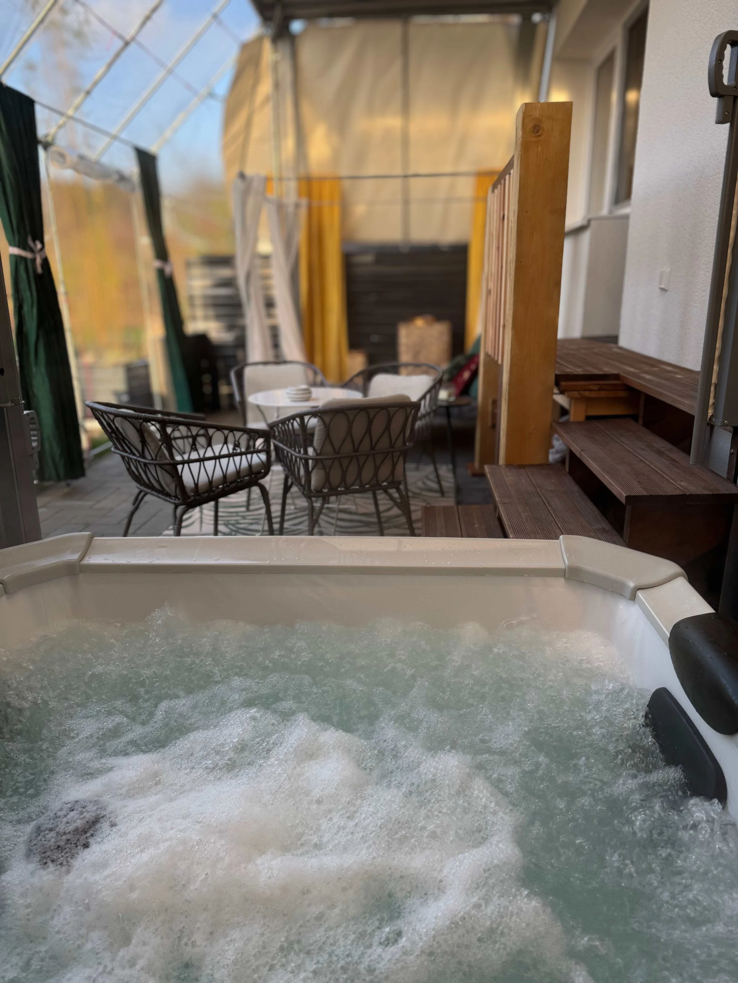 A hot tub in a semi-outdoor space with a seating area, including a round table and chairs, and a staircase on the right.