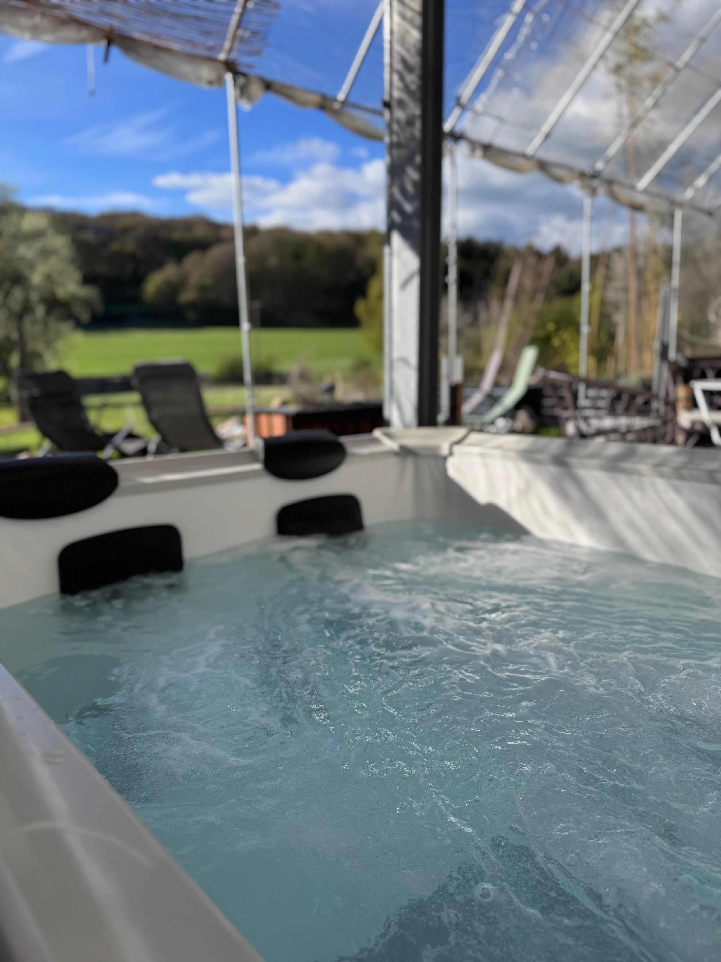 Ein modern eingerichtetes Schlafzimmer mit einem Bett, einem Wandspiegel, einer Hängeschaukel mit Kissen, einem kleinen Nachttisch mit Lampe und einem Kleiderschrank. Der Raum hat Holzfußboden und große Fenster mit Vorhängen.