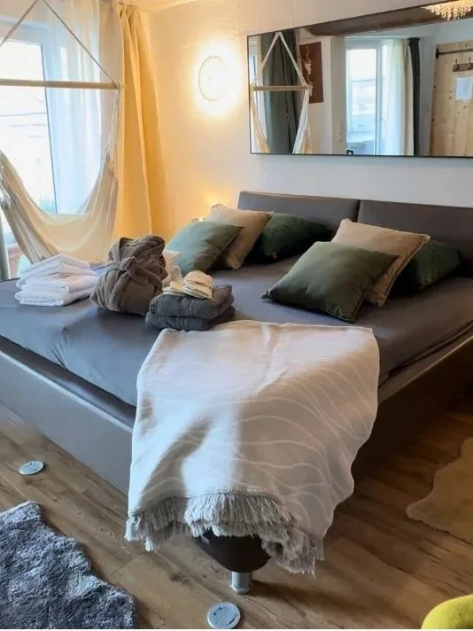Ein gemütliches Schlafzimmer mit einem aufgeräumten Bett, mehreren Kissen, einer Decke, Bademänteln, Slippern und Handtüchern.
