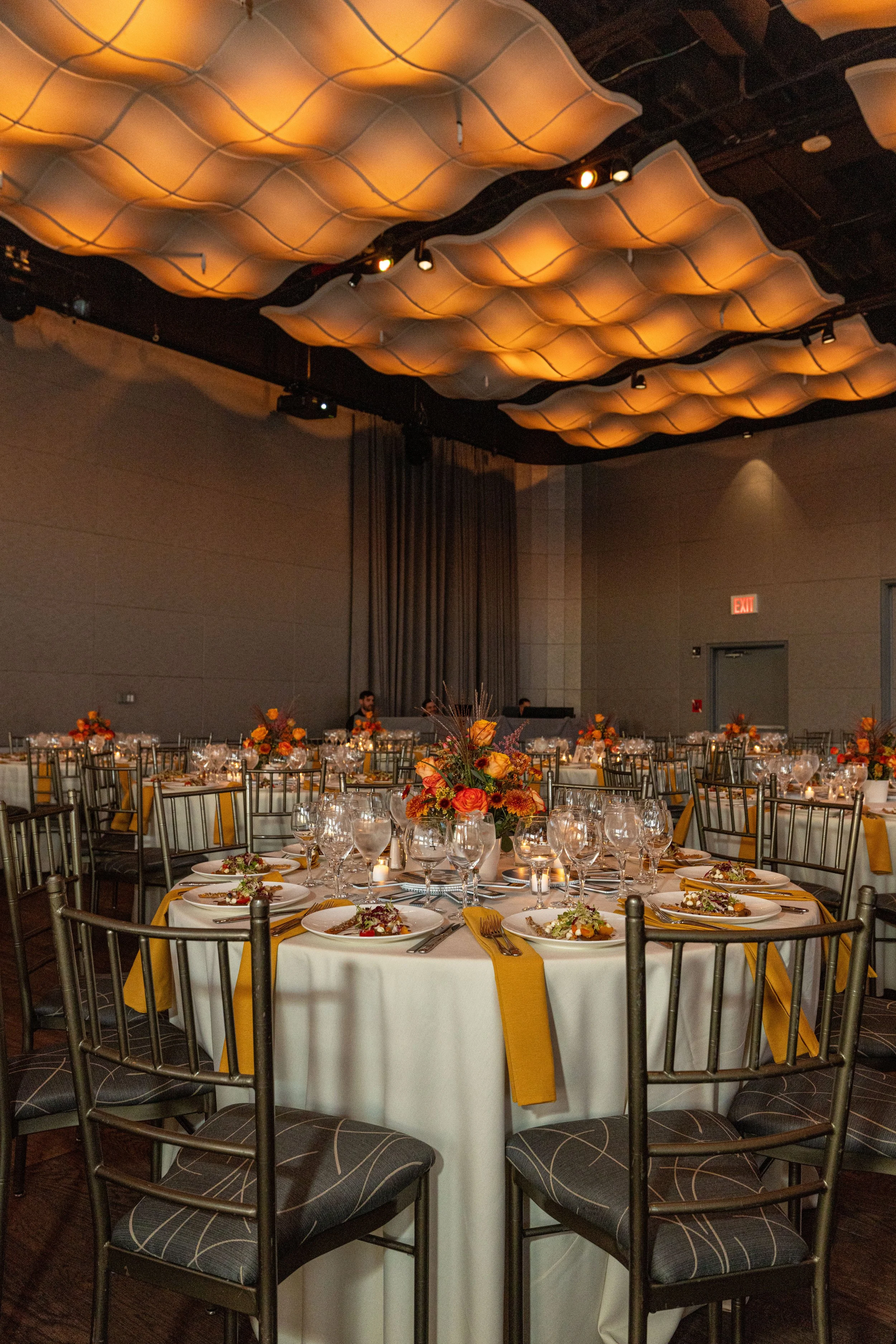 Row New York fundraising gala in an elegant banquet hall with round tables set for a formal event, decorated with yellow and orange floral centerpieces, and produced by JKM Events.