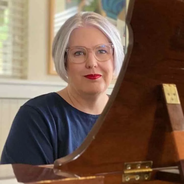 Person with short gray hair and glasses sitting near a piano.