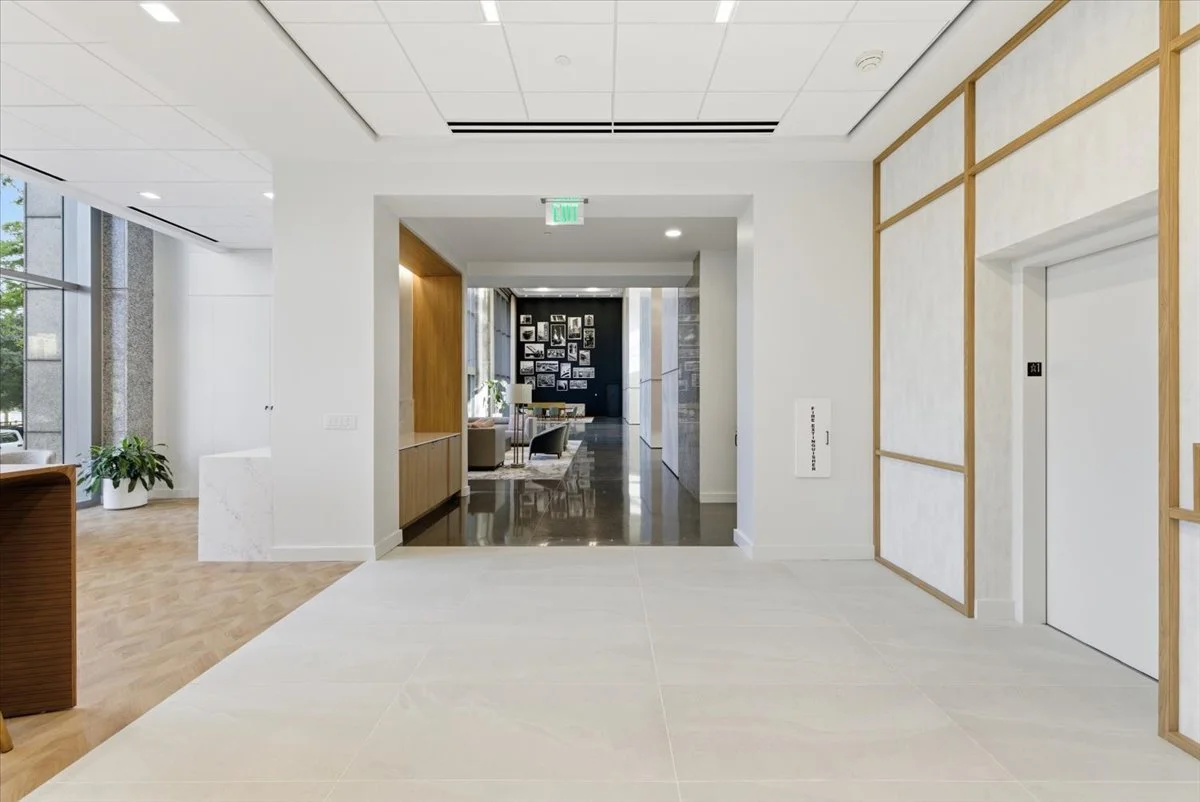 Modern, spacious entry with an elevator on the right, light-colored flooring, and a seating area visible in the background with wall art.