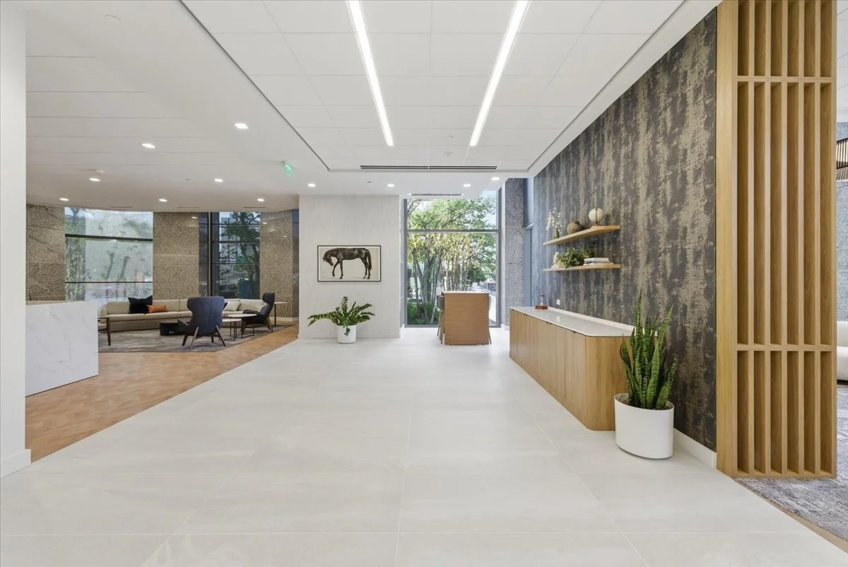 Modern tenant amenity with seating area, wooden accents, green plants, and large windows showing trees outside.